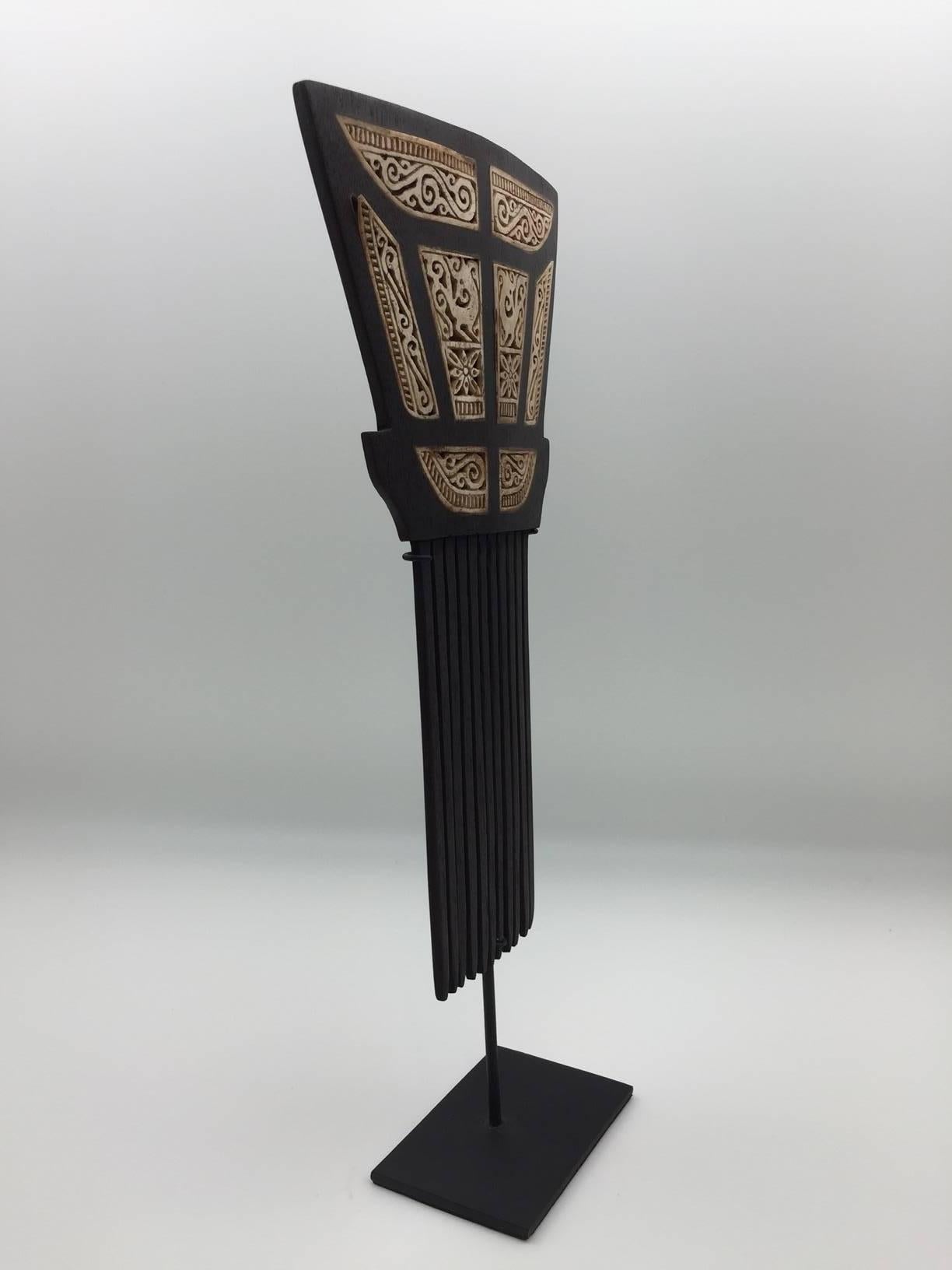 This beautifully carved wooden hair comb, inlaid with bone is from Tanimbar, which forms part of the spice islands in the Maluku province of Indonesia. It is mounted on a black painted custom metal mount. The hair comb was clearly inspired from the