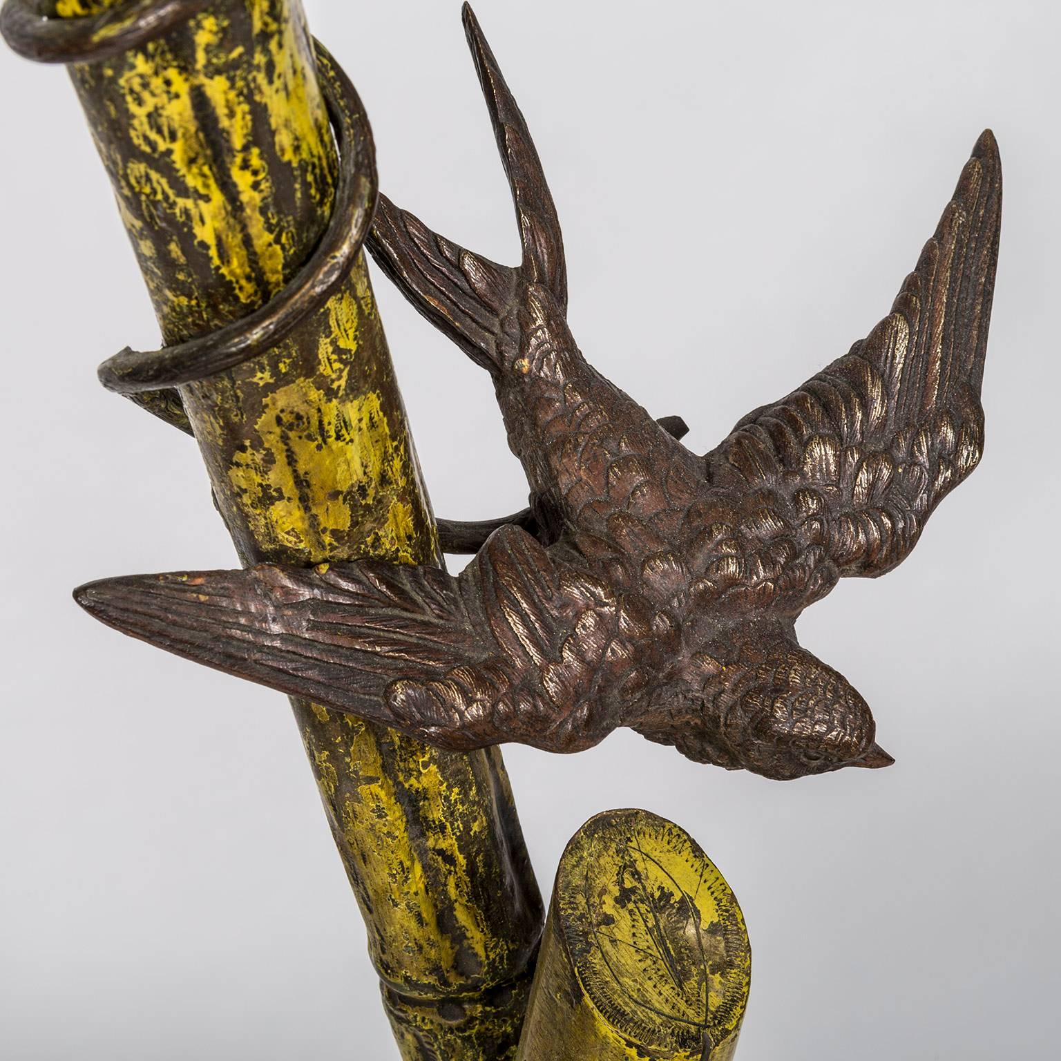 Art Nouveau Freestanding partially gilded and patinated brass stand on a three legged base depicting a water lily or nymphaea leaf and flower. The central support represents bamboo with birds depicted in flight, including a house swallow. These