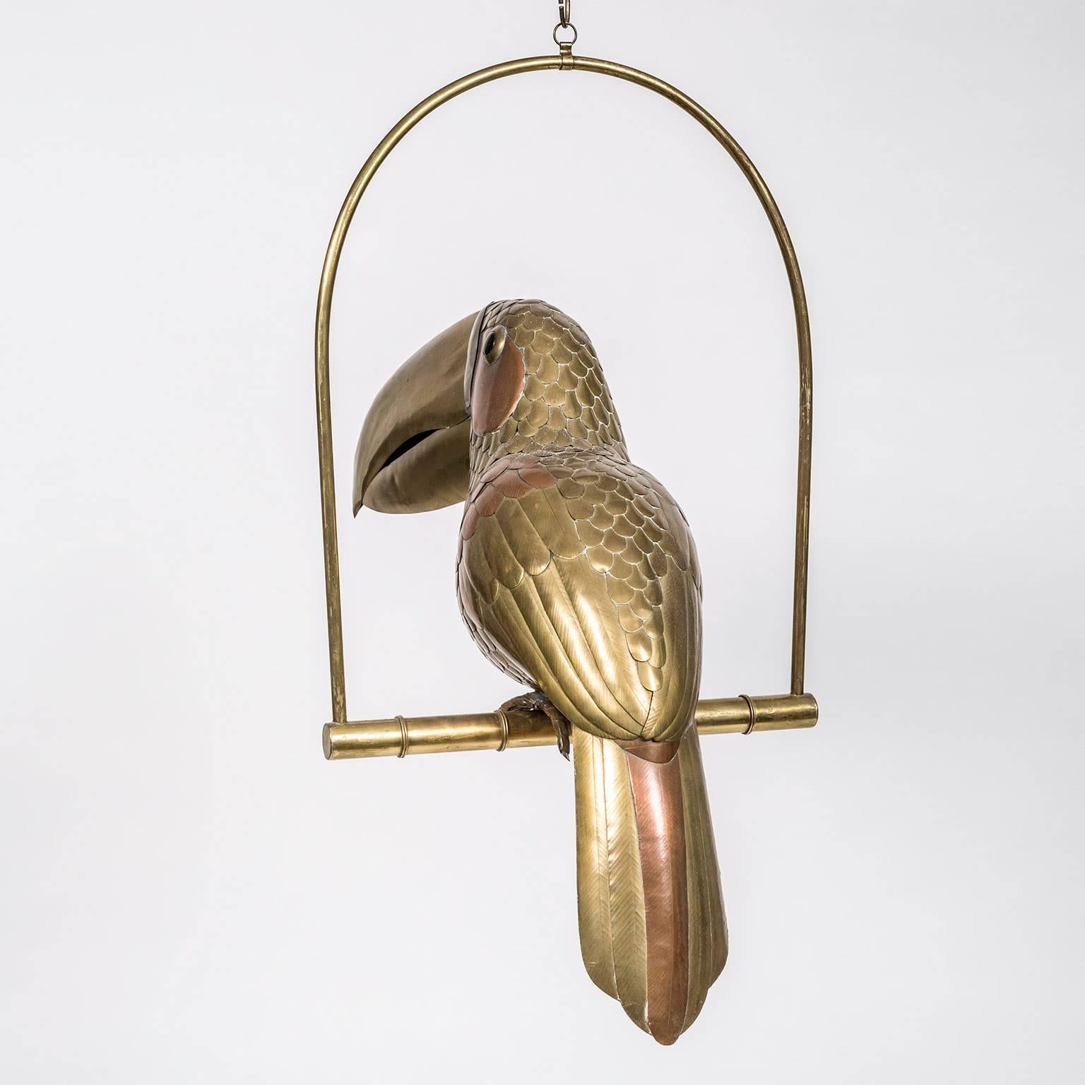 Sergio Bustamante brass and copper perched parrot with glass eyes and 11 inch brass chain to suspend from the ceiling. Executed in the 1980s by the renowned Mexican artist in his hometown of Guadalajara.