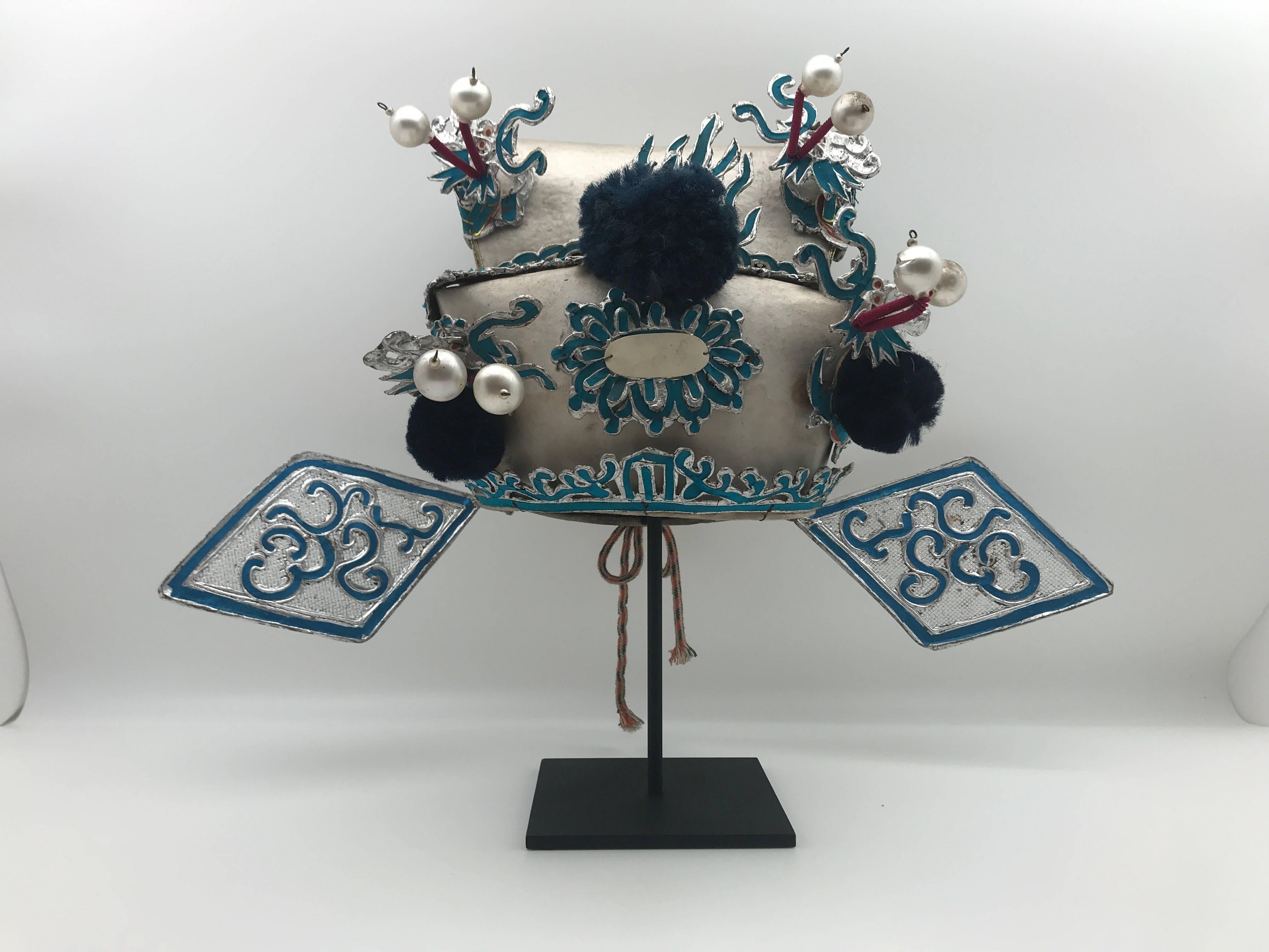 Vintage Chinese Opera theatre headdress with turquoise and white silk fabric, made to look like Kingfisher jewelry, with midnight blue pom poms. 
Early 20th century, mounted on a custom, black painted metal base.