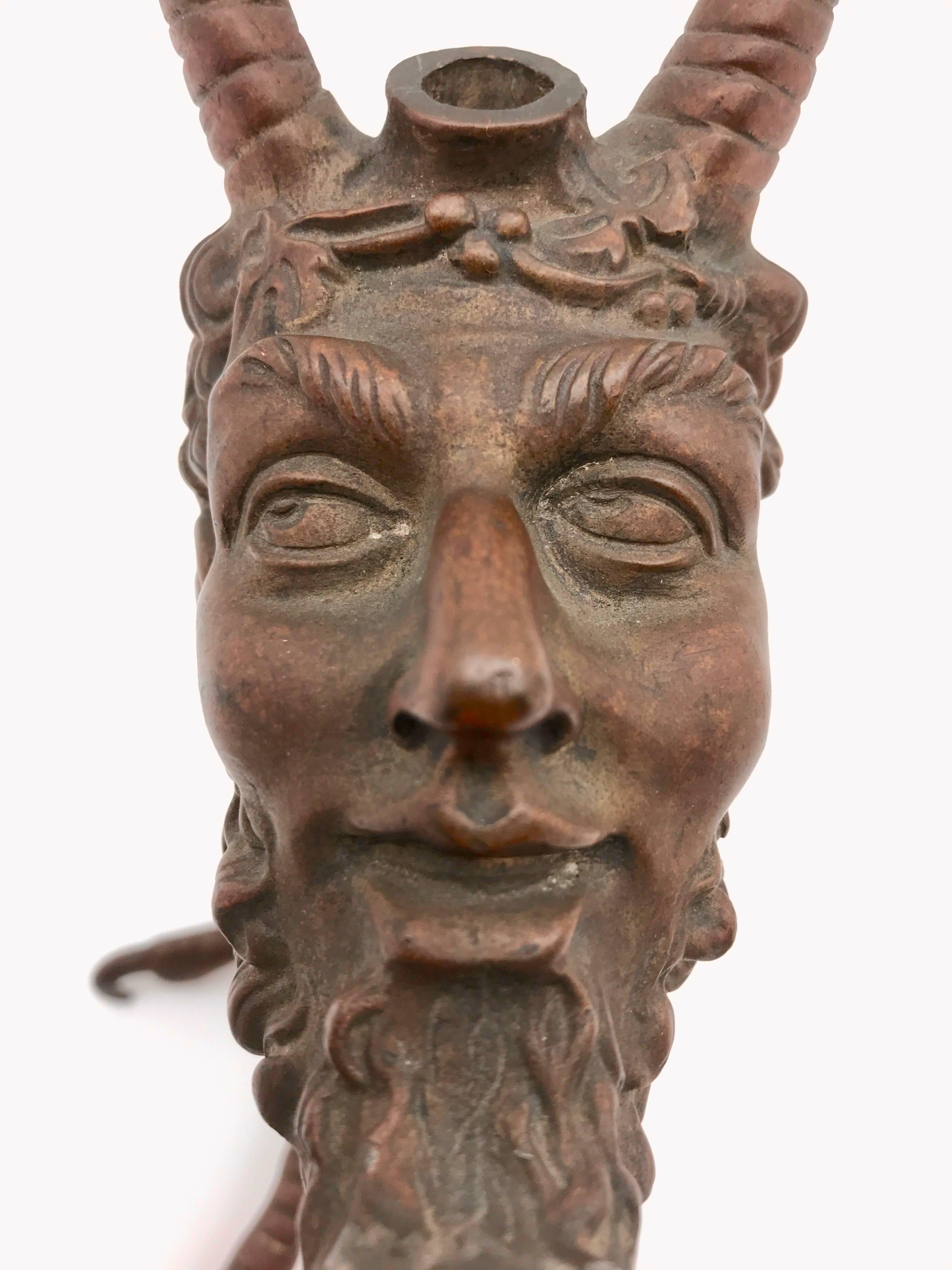 19th century continental bronze tobacco cigar lighter. The cast satyr, faun, or devil's head is mounted on a bird's claw. There is a reservoir that can be filled with oil through a hinged lid at the top of his head located between the horns. The tip