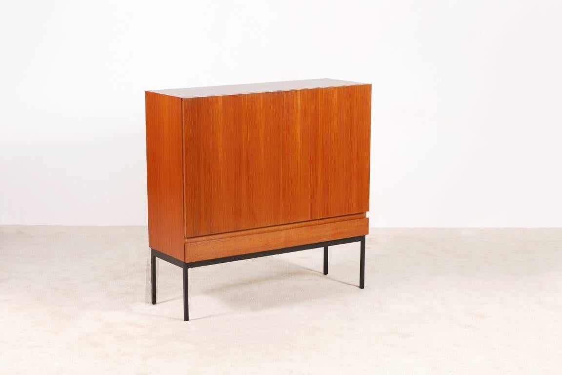 Rare double-door sideboard / cabinet designed by Dieter Waeckerlin in 1958 and produced by Behr International in the 1960s. Teak model composed of 3 shelves and 2 drawers.
Sycamore wood inside.
Black lacquered metal base.