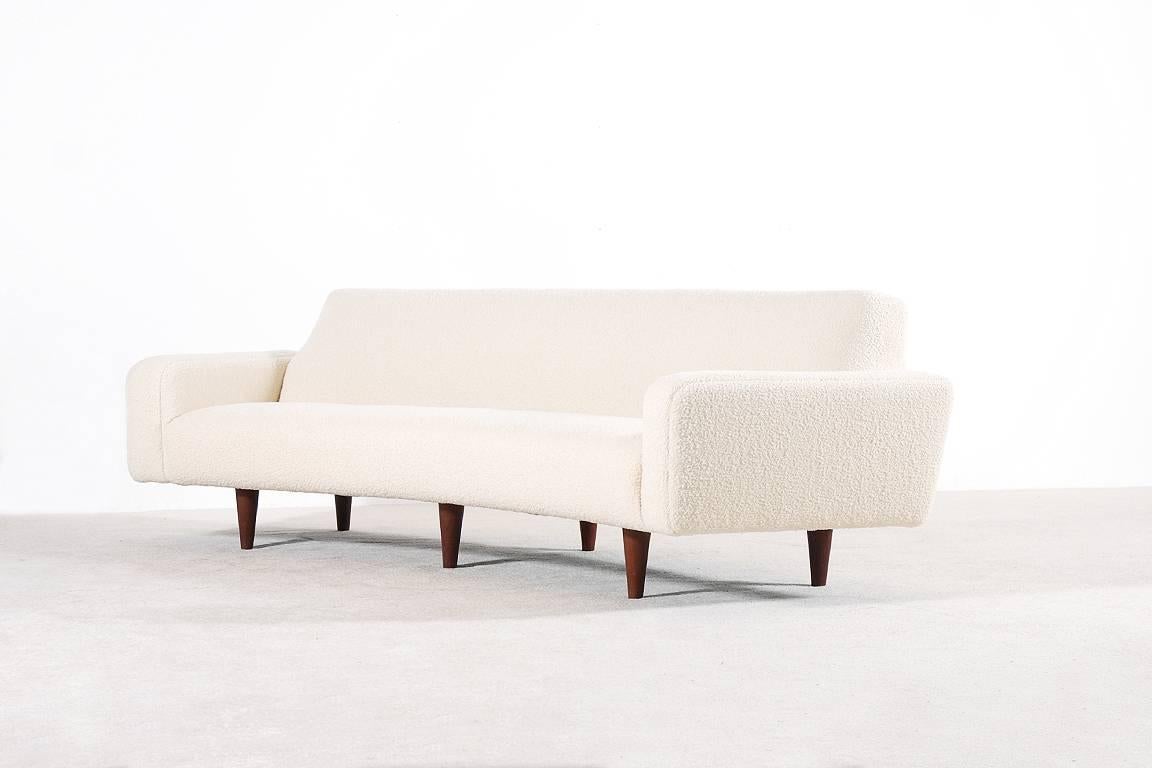 Long and curved three-seater sofa Model N°450 designed by Illum Wikkelsø, circa 1950. Produced by Aarhus Polstrermøbelfabrik.

Foam-filled and newly upholstered with a premium quality wool fabric. Ivory color. 
Teak tapered feet.

Perfect