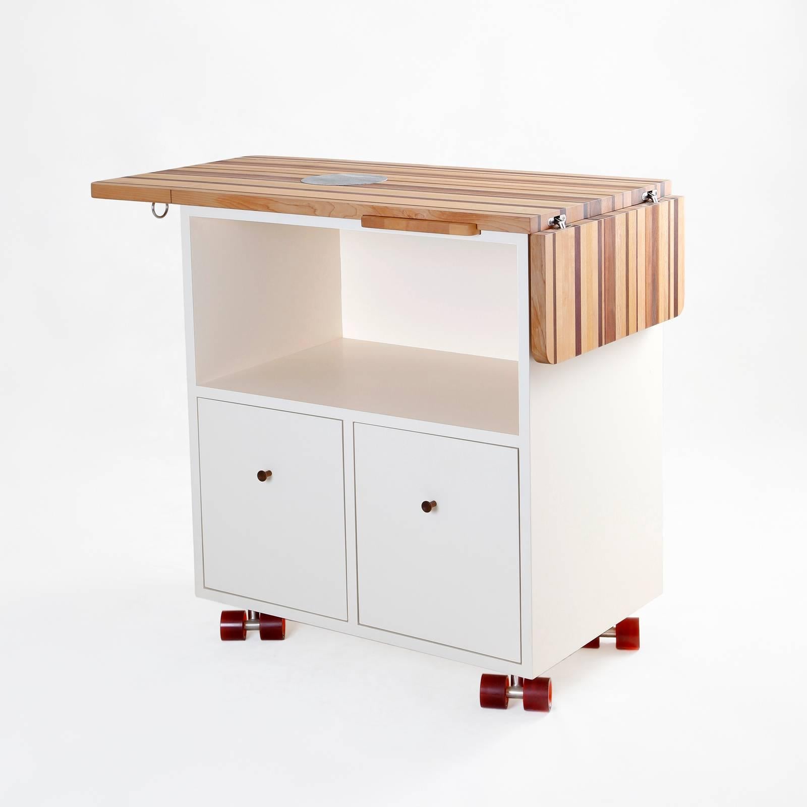 The mobile bar is meant to be flexible and multifunctional with compact storage and wood surfaces that retract. Various woods are aesthetically combined for the bar top, with ends that may be extended for a larger service area. An inlaid disk of