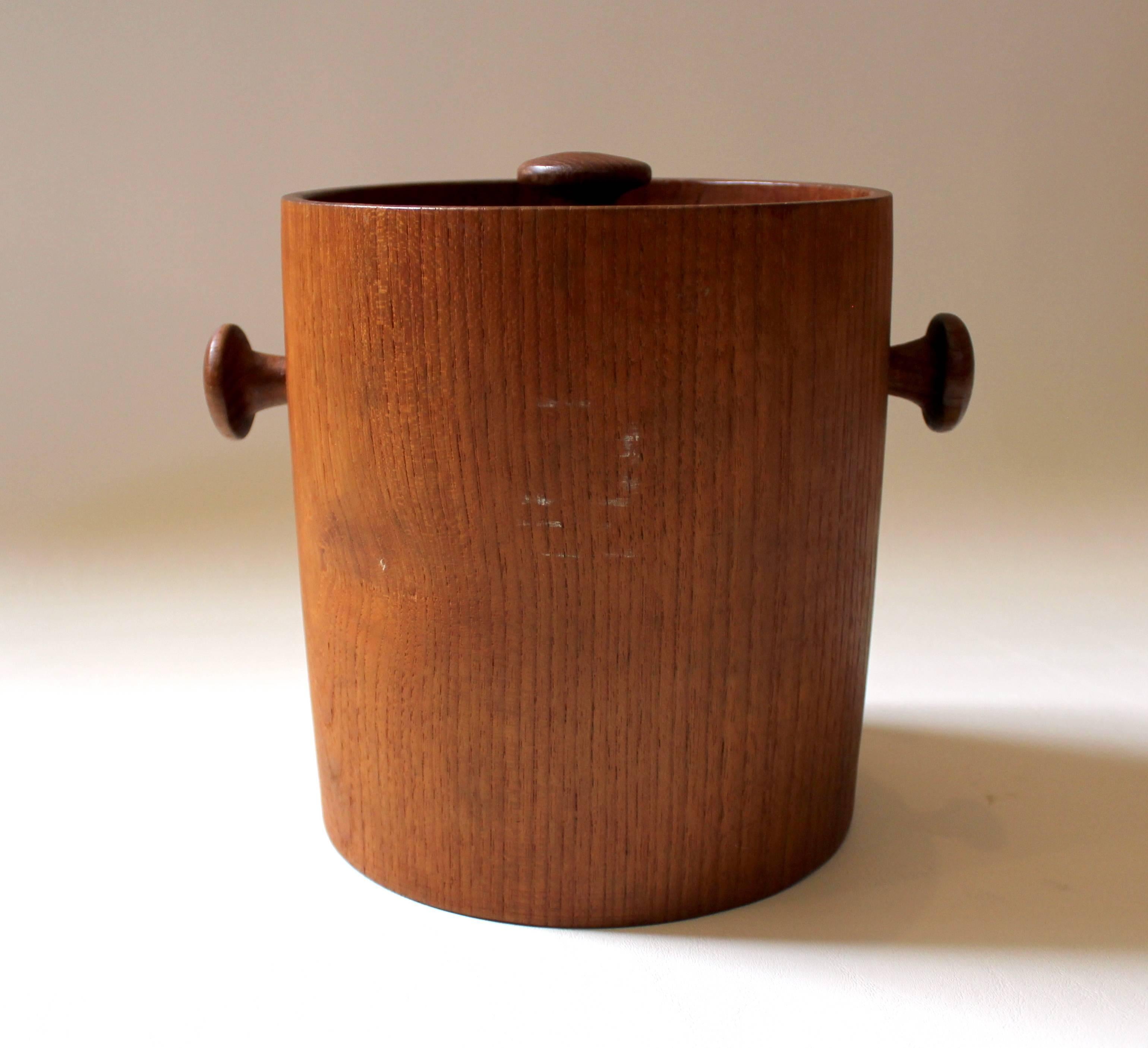 1960s Danish Modern teak ice bucket with turned handles and details. The ice bucket is solid teak, with a plastic insulation liner. In excellent condition.