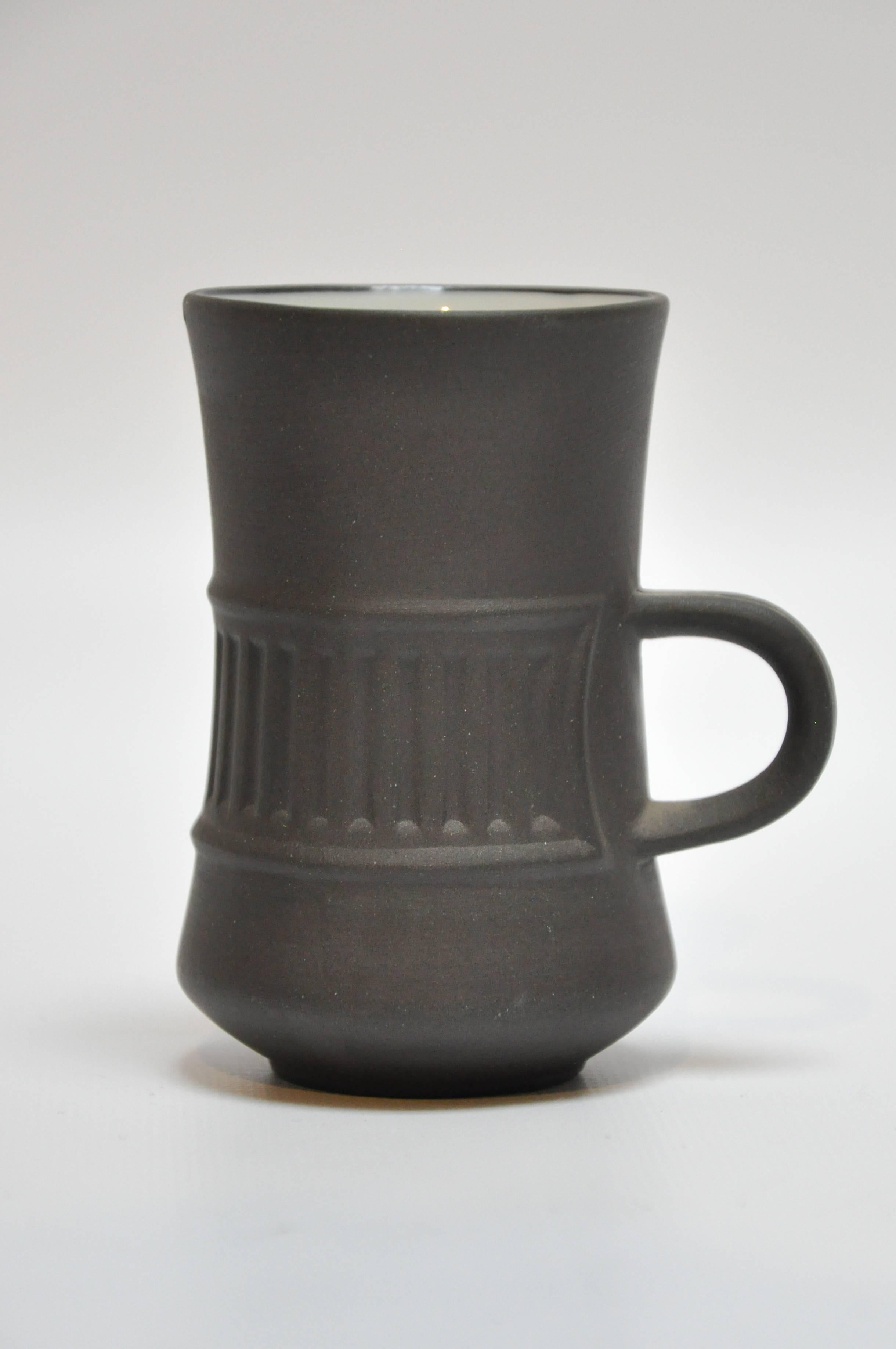 Mid-Century flamestone coffee set by Jens Quistgaard for Dansk. The set consists of ten espresso cups and saucers and a large coffee pot with lid. The exteriors are a dark matte gray and the interiors a glazed off-white. Stamped 