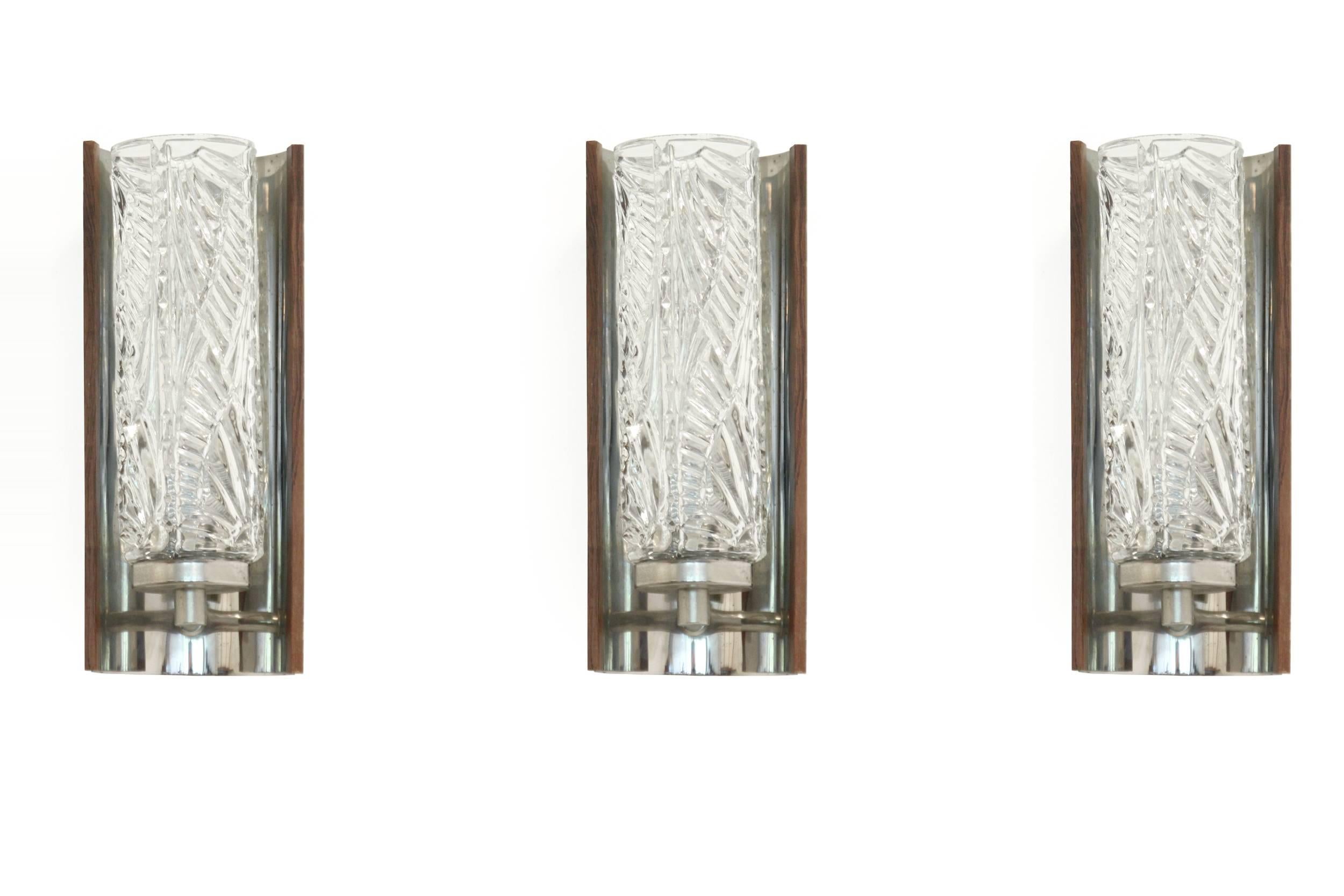 Set of three wall lights on a chromed frame with rosewood details and crystalized glass shades.

Most likely designed and made in Denmark ca 1970s second half.

All lamps are fully working and in good vintage condition.