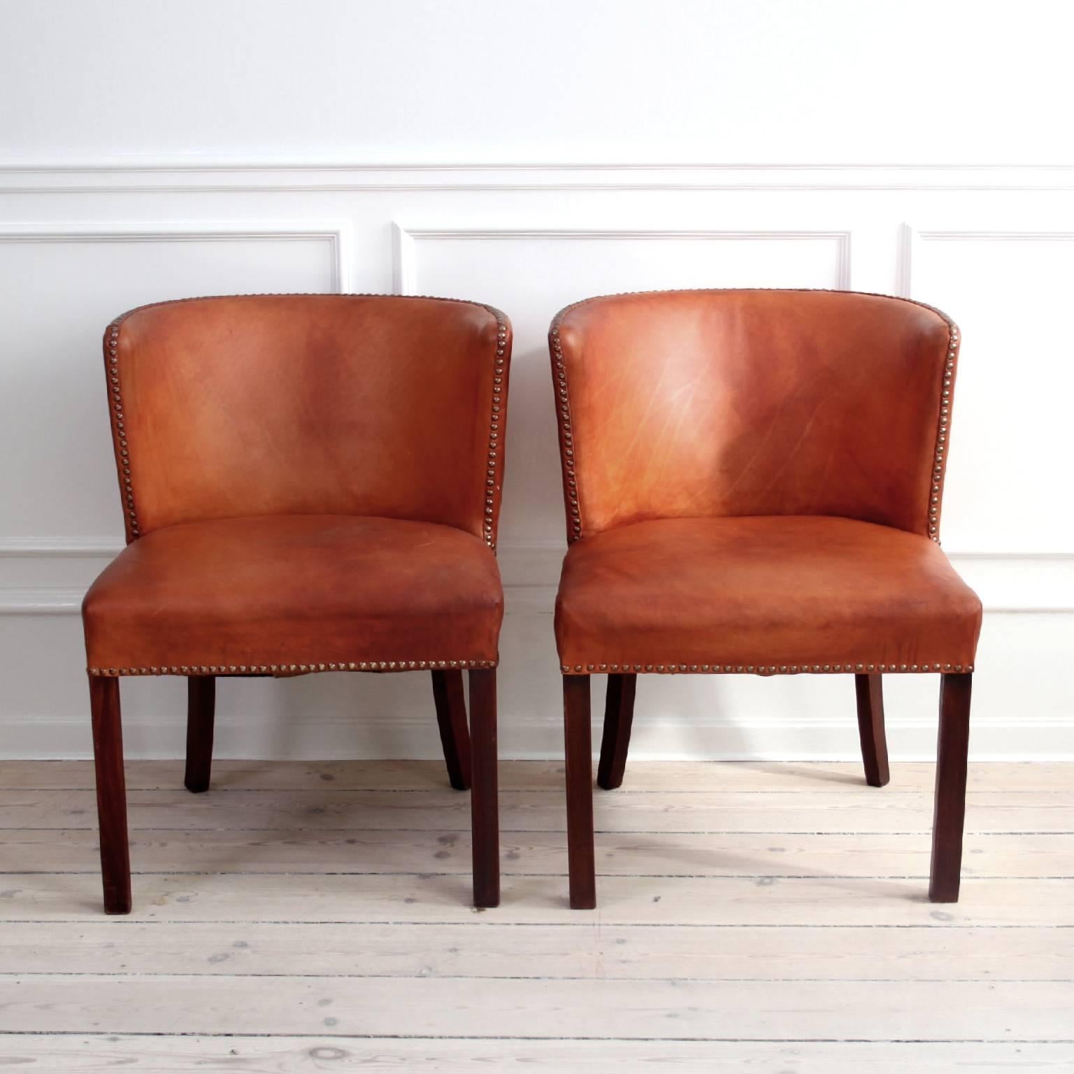 FRITS HENNINGSEN. 

Pair of chairs, designed and manufactured by Frits Henningsen, Denmark, 1930s.

Materials: Natural leather with a beautiful Cognac coloured patina, mahogany and brass nailheads.

Size: 75 x 55 x 55cm.

Excellent vintage