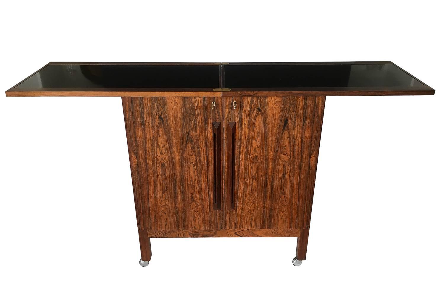 Desirable rosewood bar cabinet designed by Torbjørn Afdal for Bruksbo of Norway. Locking cabinet opens to reveal storage for all necessary bar accoutrements. Black laminate flip-top doubles in size for additional working space. Bar is complete with