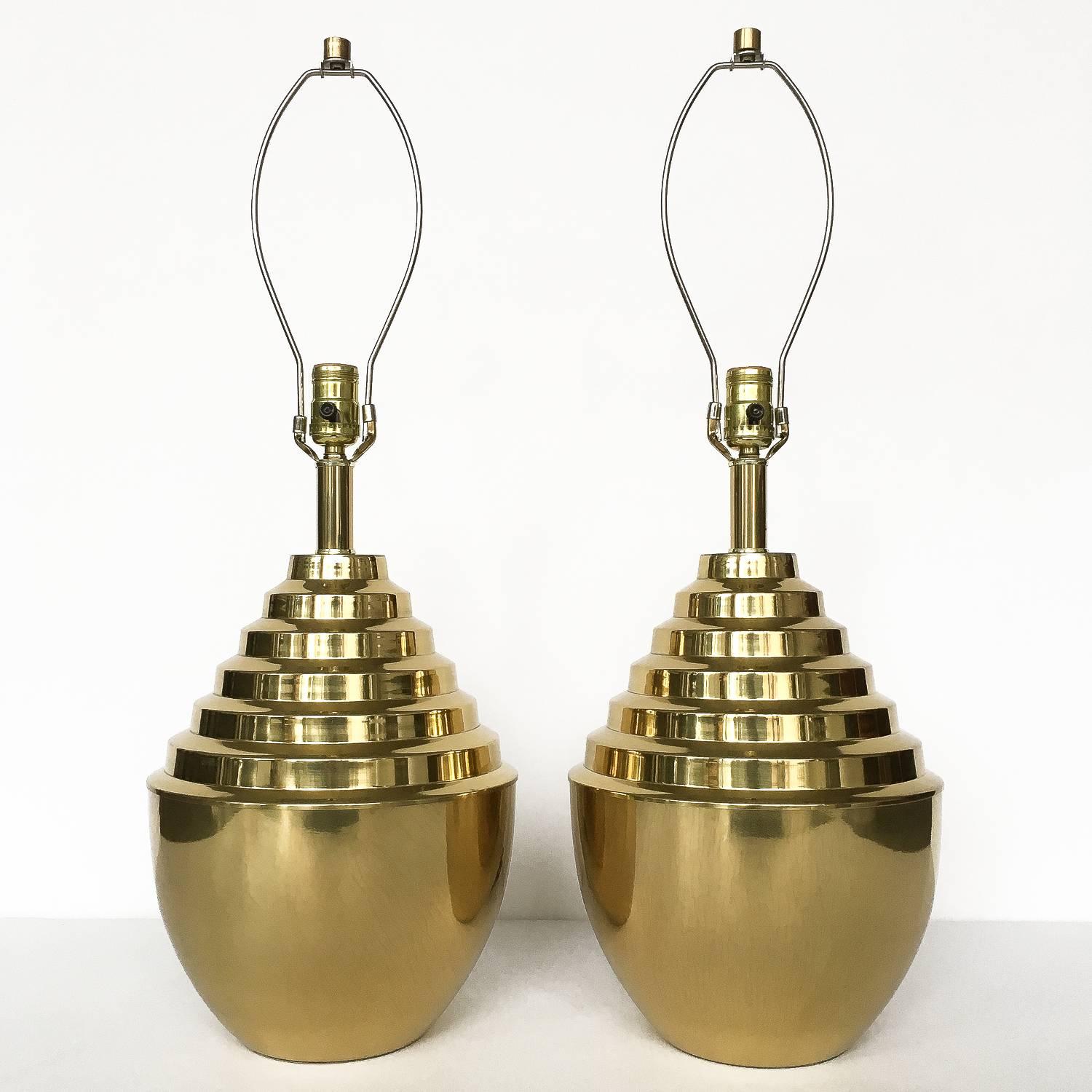 Unique striking pair of sculptural brass table lamps. Rounded urn-form base with modernist stepped design, circa 1970s. Solid brass cylinder finials. Sold sans shades. Working condition.