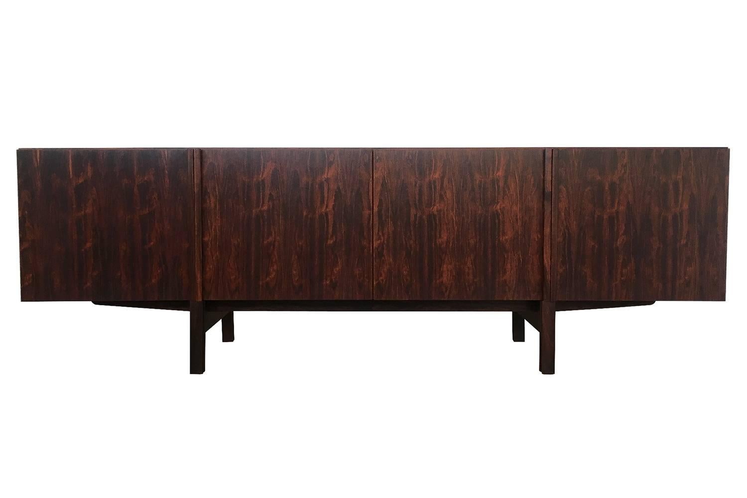 Rosewood sideboard or credenza by Ib Kofod Larsen for Faarup Mobelfabrik, circa 1960s. Featuring four hinged doors with carved rosewood handles that visually integrate vertically into the legs. The interior of the cabinet has four rosewood felt