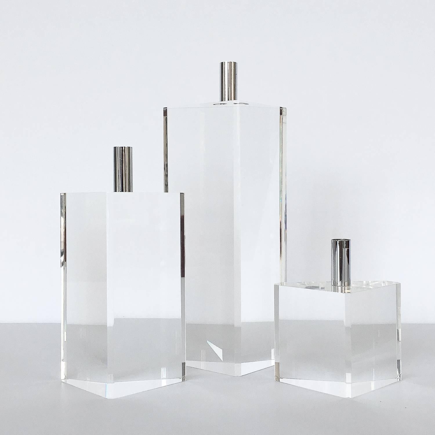 Set of three faceted solid Lucite and chrome candlesticks. Set of three graduated triangular shaped solid Lucite candle holders with chrome cylindrical cups. Chrome cylinders measure 1.25