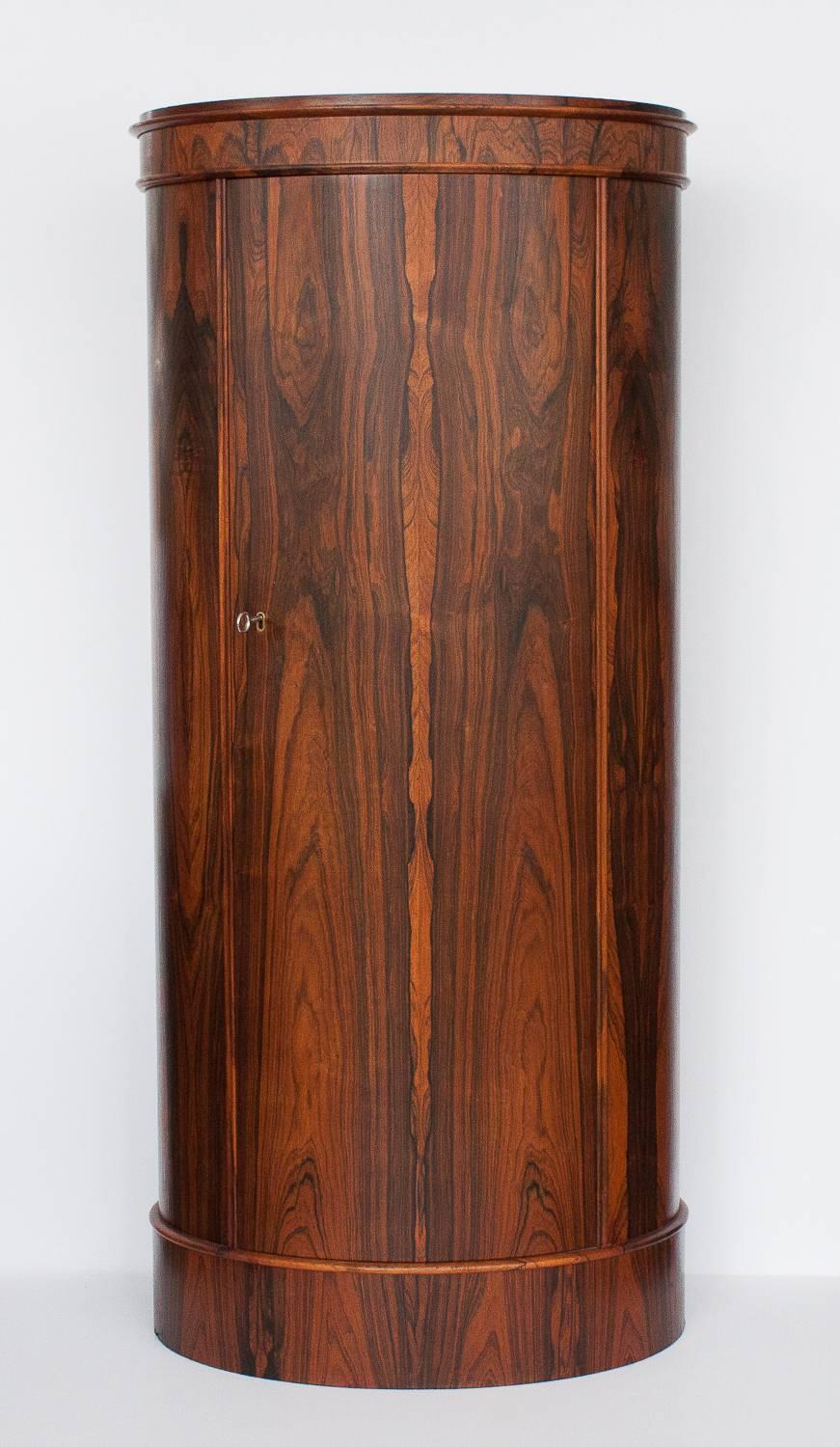Oval shaped Brazilian rosewood pedestal cabinet designed by Johannes Sorth and produced by Bornholms Moblefabrik, Denmark in 1960.  The cabinet features 6 adjustable interior shelves and locking keyed mechanism.  Stunning grain patterning to