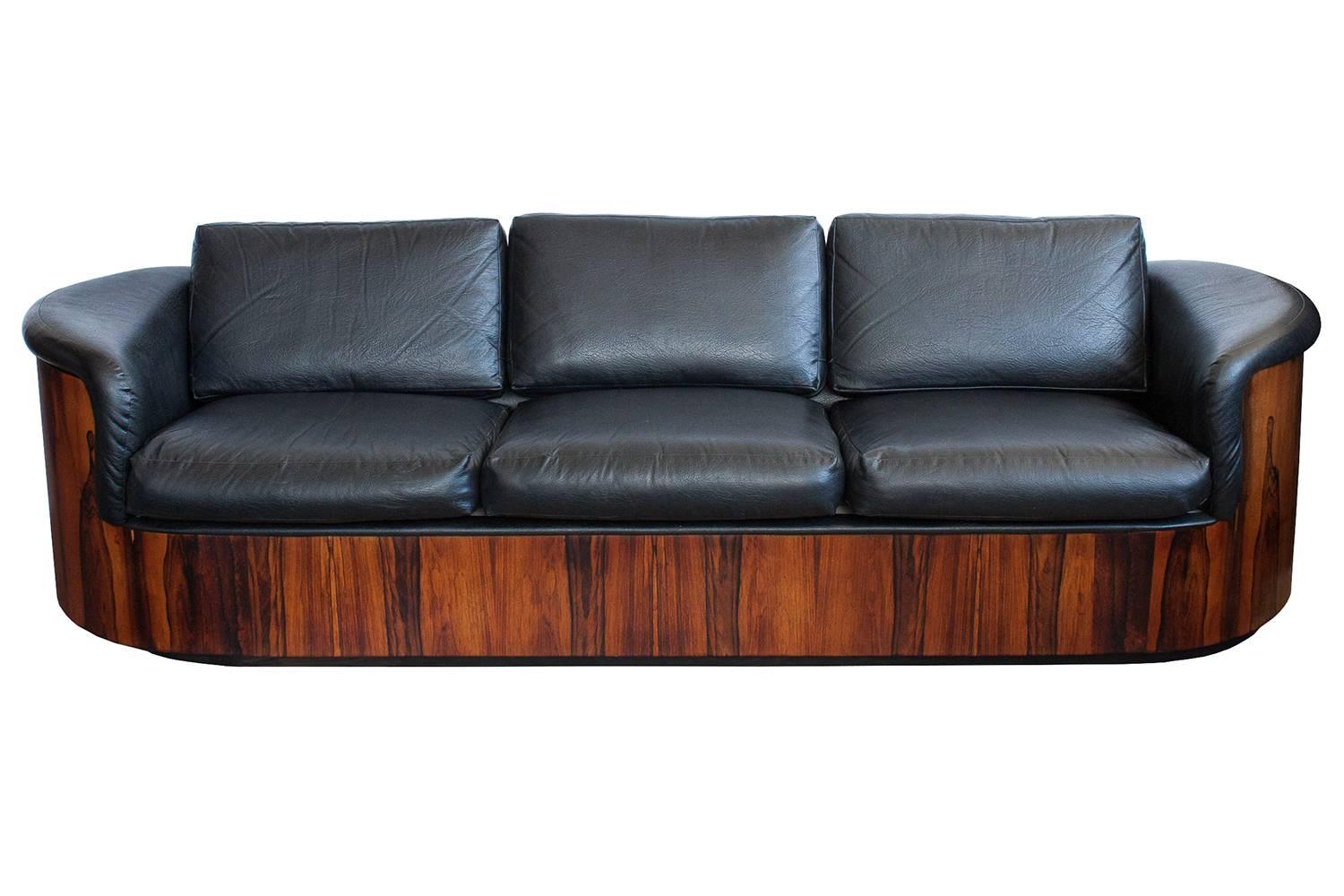 Rare rosewood sofa by Plycraft. A seldom seen design by Plycraft, one of the pioneers of moulded plywood furniture in America. Nicely figured grained rosewood and original black naugahyde upholstery. Unique racetrack/pill shaped moulded plywood
