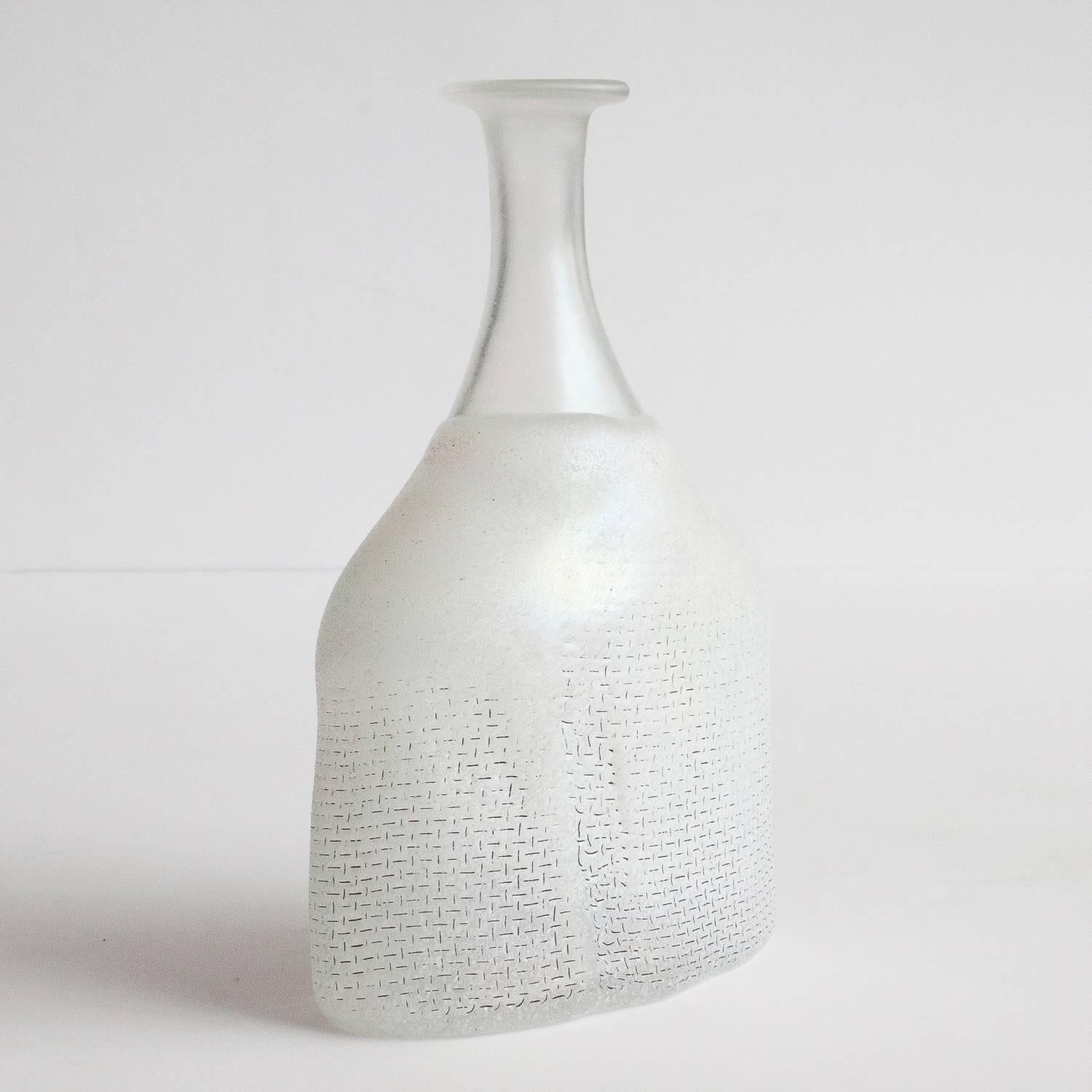 Bertil Vallien vase / bottle in the series Network for Kosta Boda. Designed in 1979. The design is called Network and is handblown. The series got its ruff net pattern when the glass is blown into a mould lined by steel mesh. The glass is white /