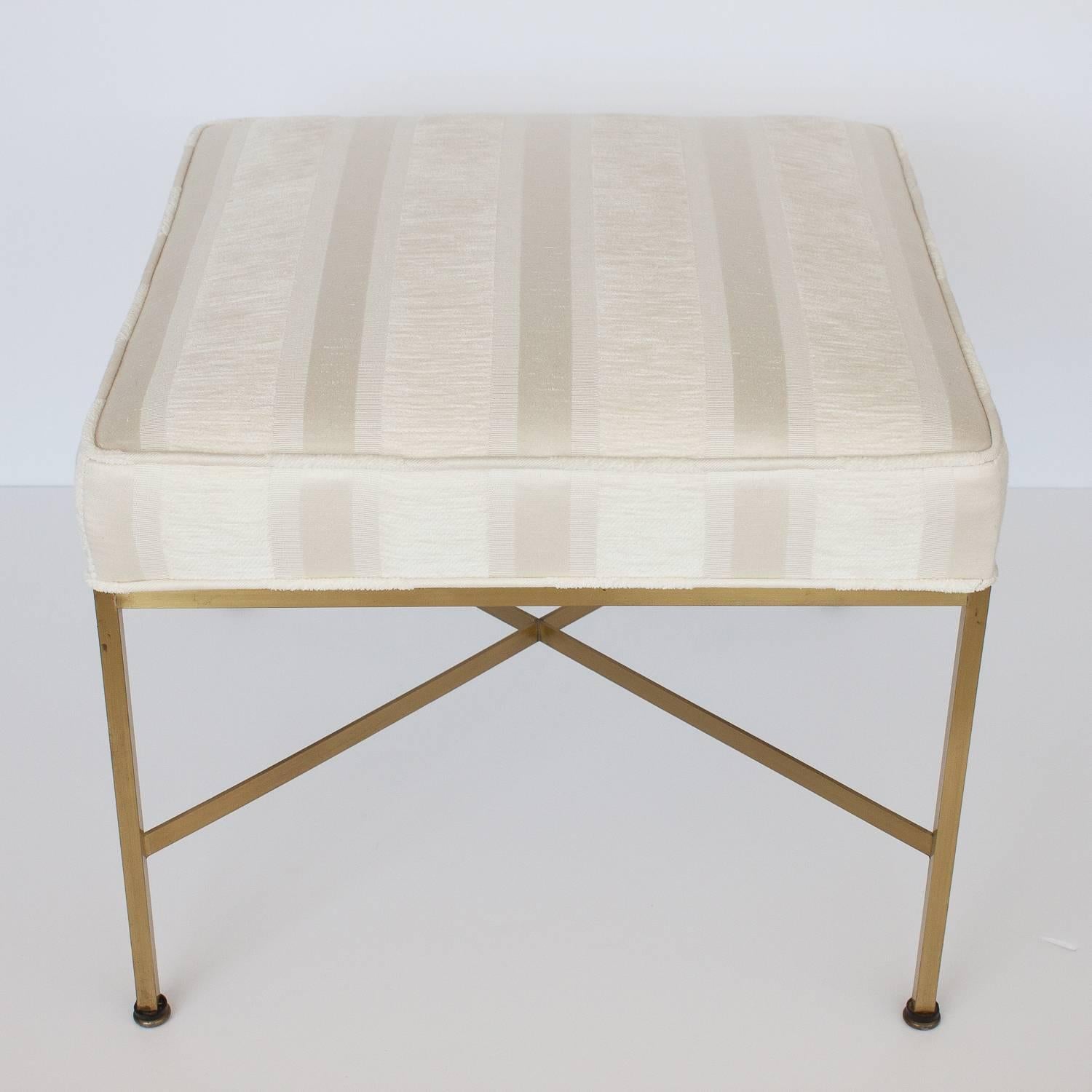 Paul McCobb ottoman / foot stool with X shaped stretchers in brass. Square upholstered seats supported by a slim brass frame. Ivory chenille and sateen stripe fabric. General patina to brass finish.

