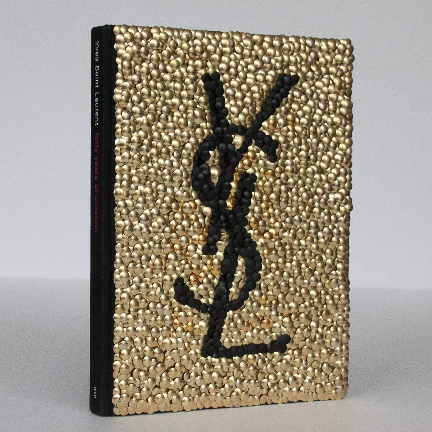 Hand gilded copy of Yves Saint Laurent - 40 years of creation fashion art book with brass and painted black thumbtacks forming the YSL logo on the front cover by Chicago artist Brian Stanziale. 

Sculptural and playful, 