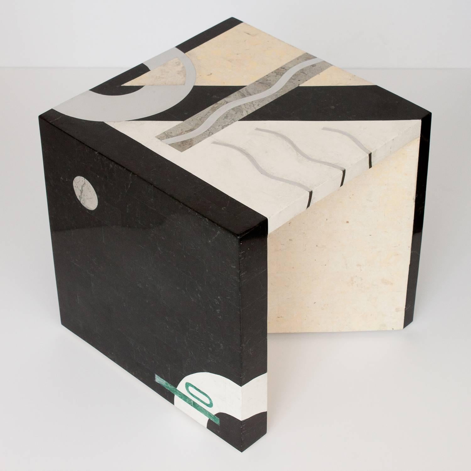 Striking modern Italian tessellated marble side or end table by Oggetti. Geometric abstract design. Sculptural form with unexpected diagonal leg opening the cube on two sides. Stone veneer in black, off-white, cream, gray and a touch of green.