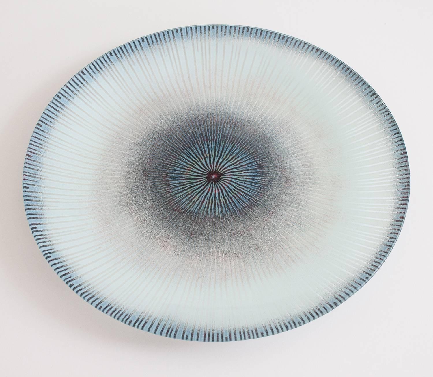 Maurice Heaton (1900-1990) enameled glass charger with sunburst design in pale blues and a touch of red. Signed M.H. In 1947, Heaton invented a process of fusing crystals of enamel to glass surfaces, allowing for rich experimentation for