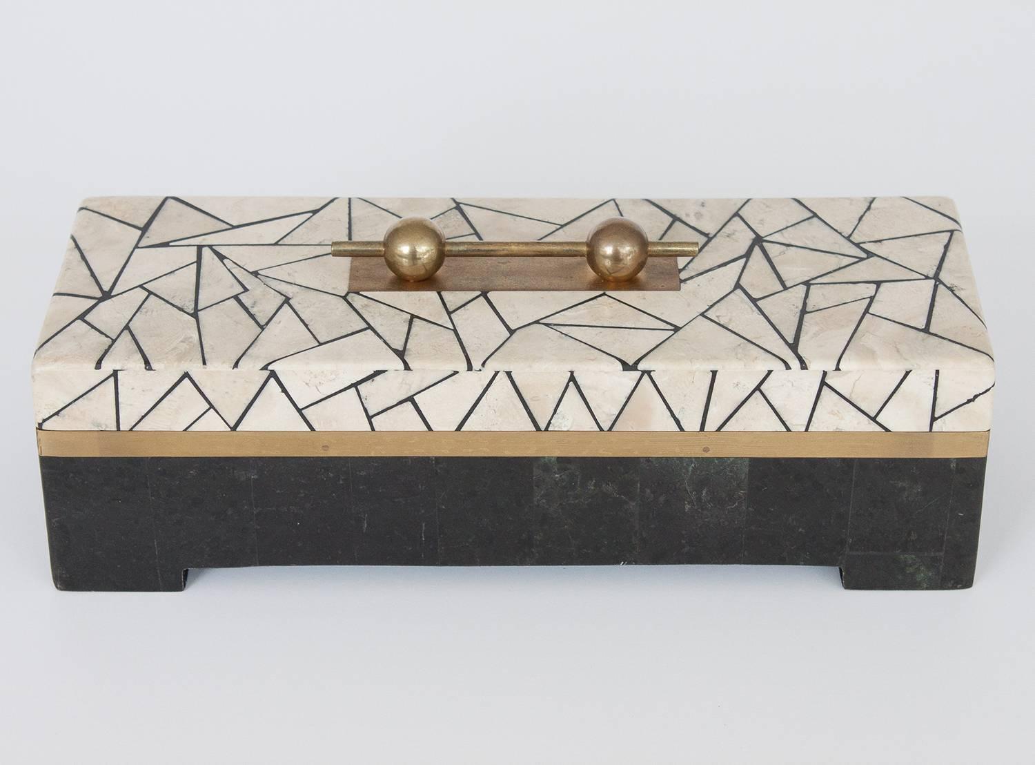 A large tessellated stone box by Maitland-Smith. Unique and bold ivory and black asymmetrical faceted geometric design. Comprised of two stone veneers in black and ivory. Inset brass banding and brass ornamental handle. A hinged top opens to reveal