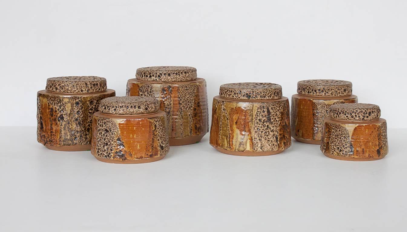 The handmade earthenware canisters are glazed in earthtones of brown, tan, orange and yellow. A unique thick porous lava glaze is incorporated on the canister body and completely covers each lid. The interiors of the canisters are also glazed. Each