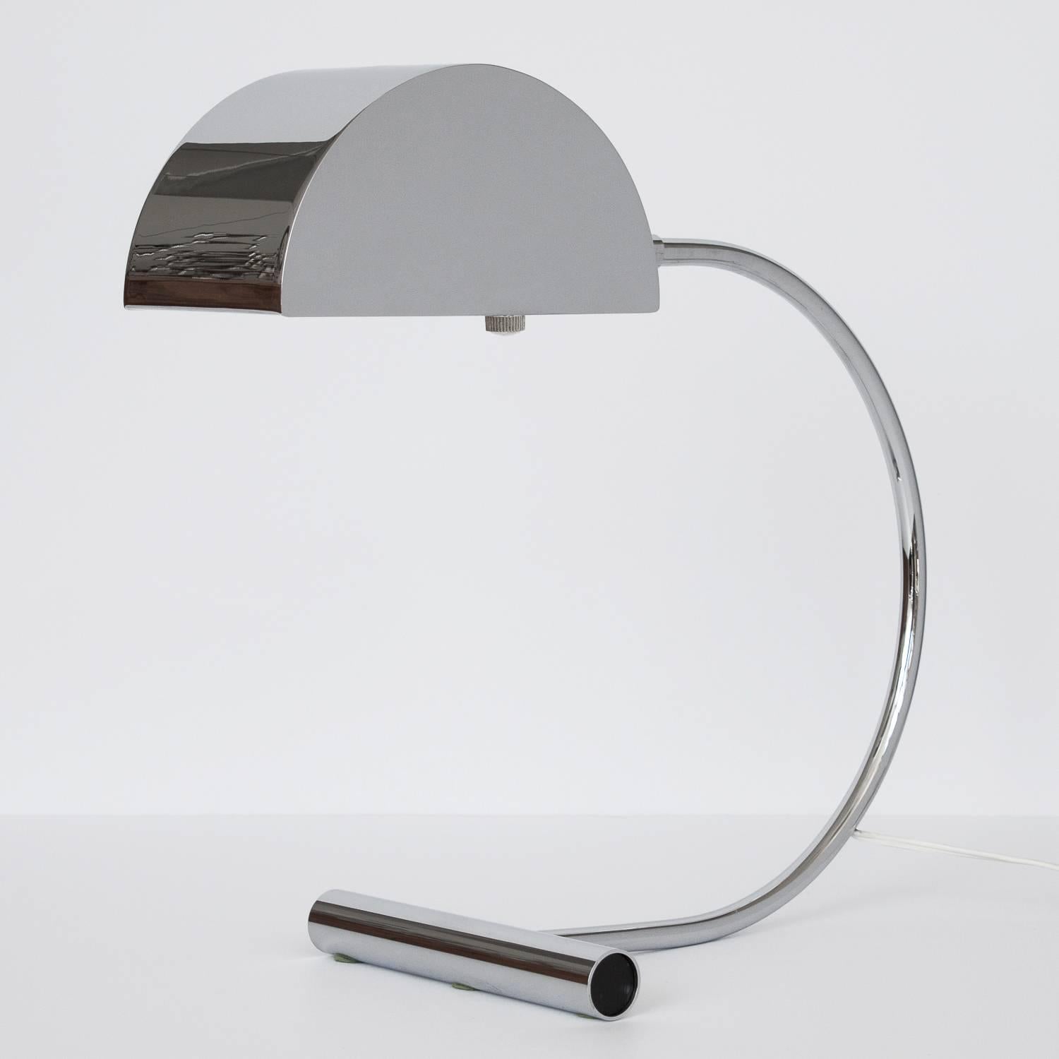 Koch and Lowy polished chrome cantilevered desk lamp. Weighted cylinder base with curved arm that supports a half cylinder chrome shade. Adjustable shade / lamp head. Takes one standard light bulb. Dimmable switch located on socket. Working