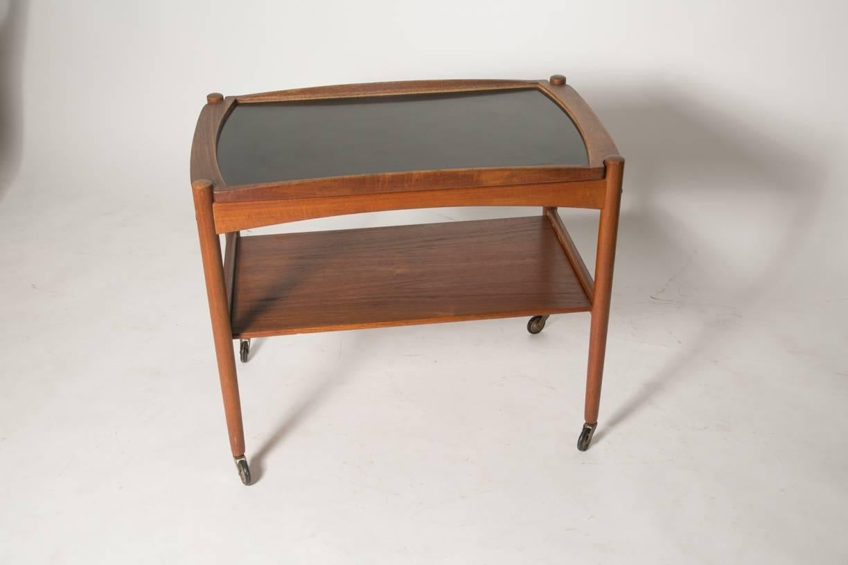 Versatile and stylish teak bar cart with removable tray top, low shelf and brass wheels. Design reminds us of Danish Mid-Century designer Poul Hundevad. Tray features durable black formica and curved teak rails that set in to the frame. Very good