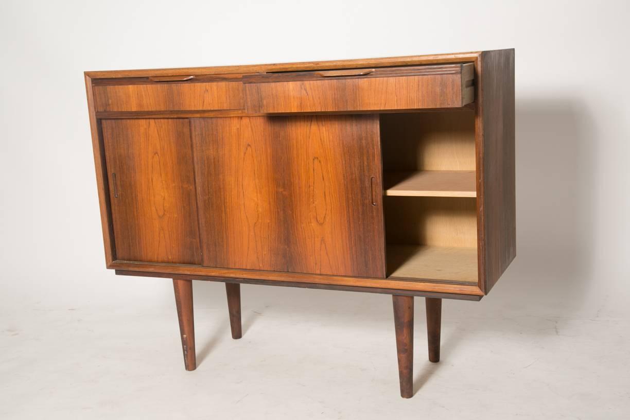 Apartment sized old growth rosewood sideboard. Slender tab pulls open the two felt lined drawers and sliding doors open to reveal shelving. Elegant minimal design with stunning contrast and grain in the rosewood.
