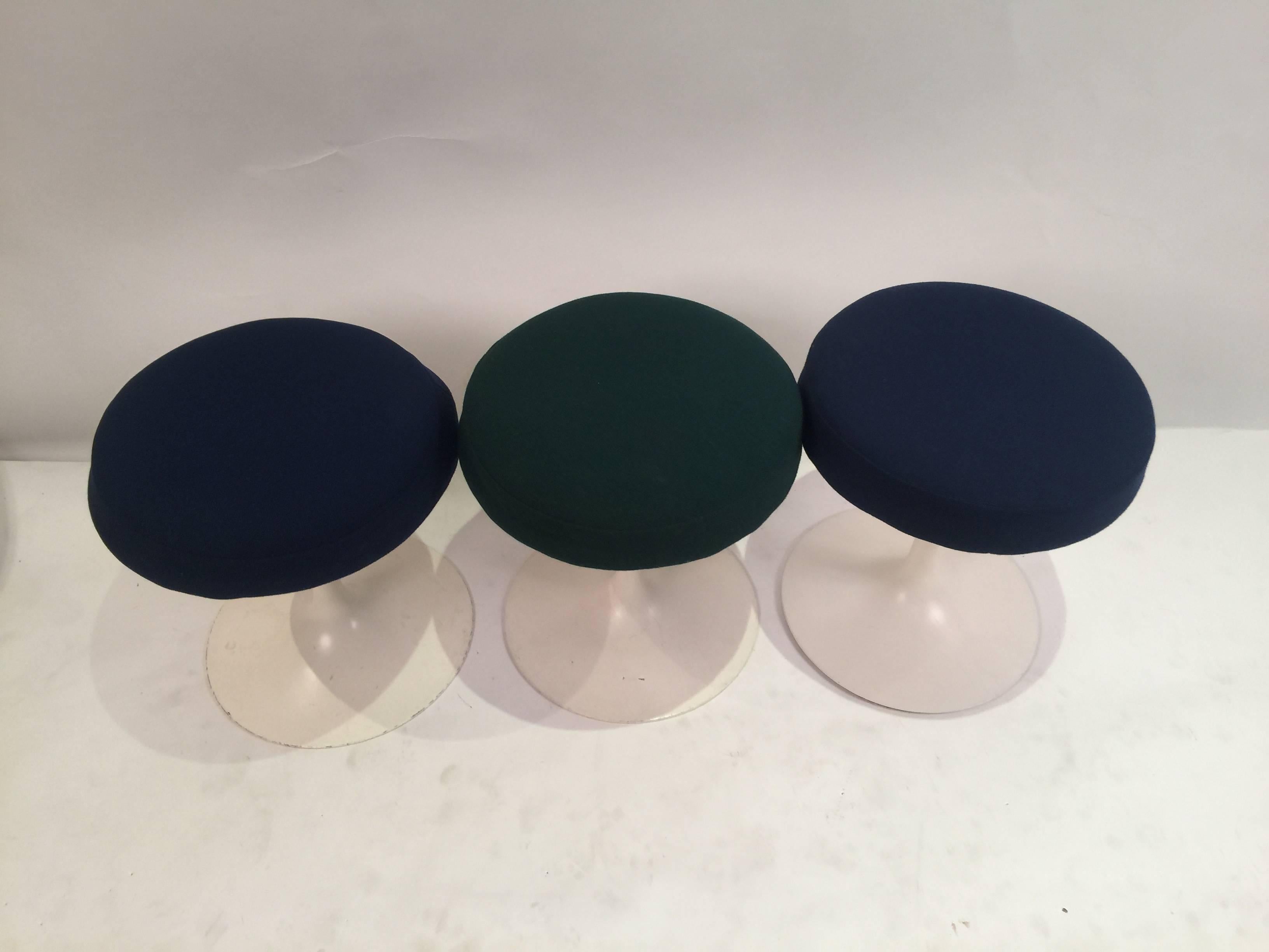 Set of three tulip stools designed by Eero Saarinen in 1956 for Knoll. Two of them are upholstered with navy blue fabric and the third one with dark green fabric. Stools bear original paper and fabric labels. Metal base marked with early