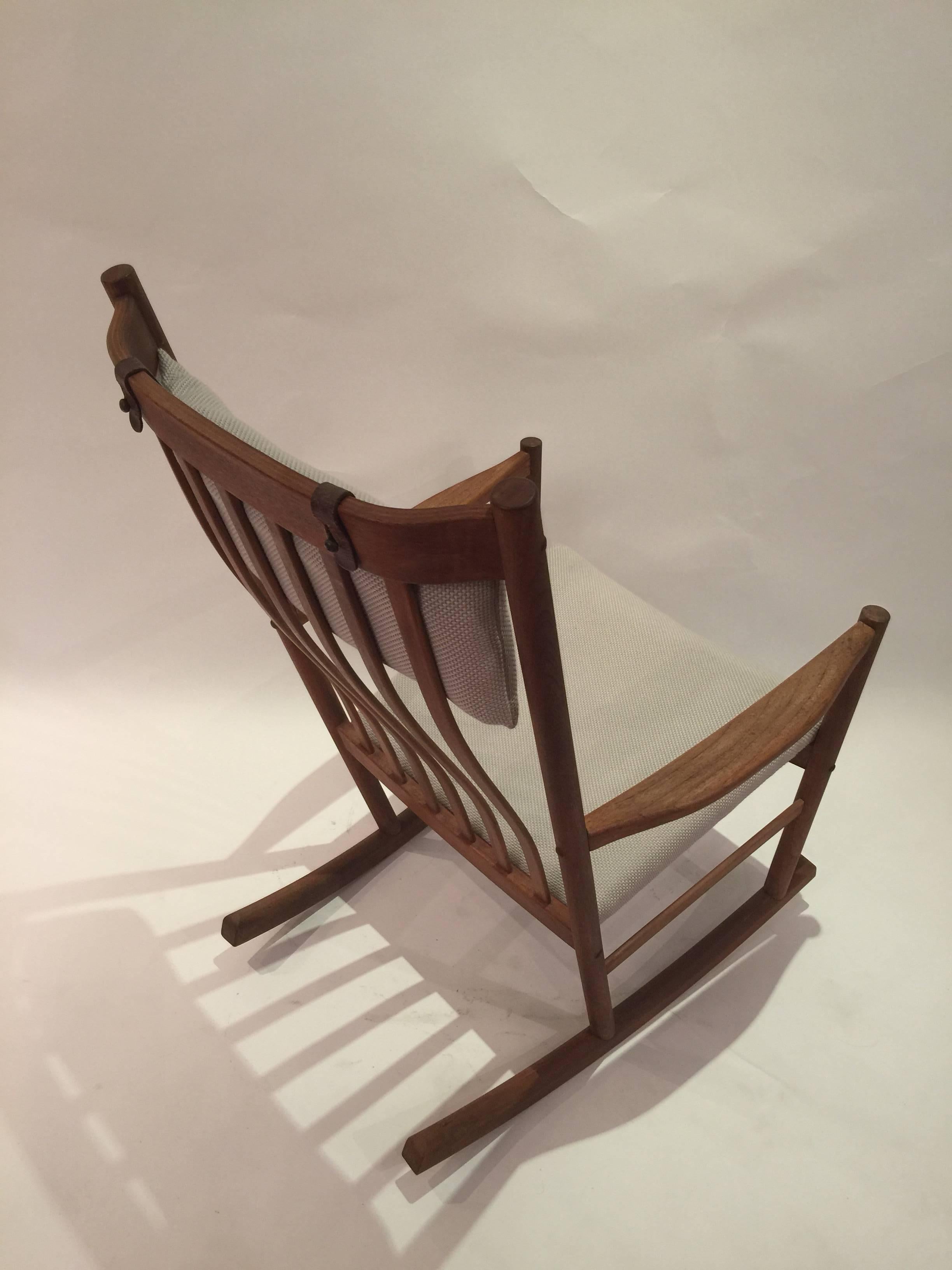 High back rocking chair with simple design and attention to detail by designer Hans Wegner for manufacturer Tarm Stole. Steam bent teak slat back and newly reupholstered in white and cream opalescent cotton woven fabric.