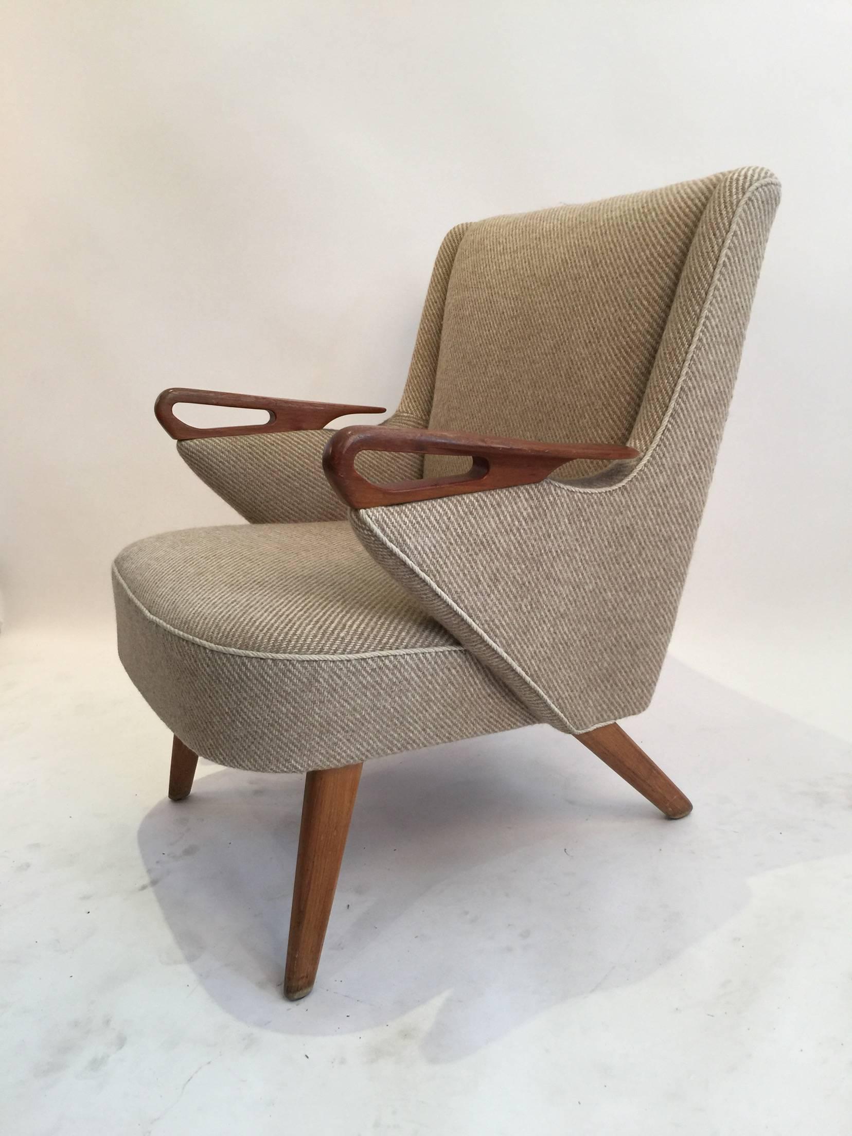 This Danish lounge chair is a unique piece from the Mid-Century Scandinavian Modern era. It is in its original two-tone beige wool twill upholstery and piping, features a flared back, teak legs and beautifully carved teak armrests. The design is
