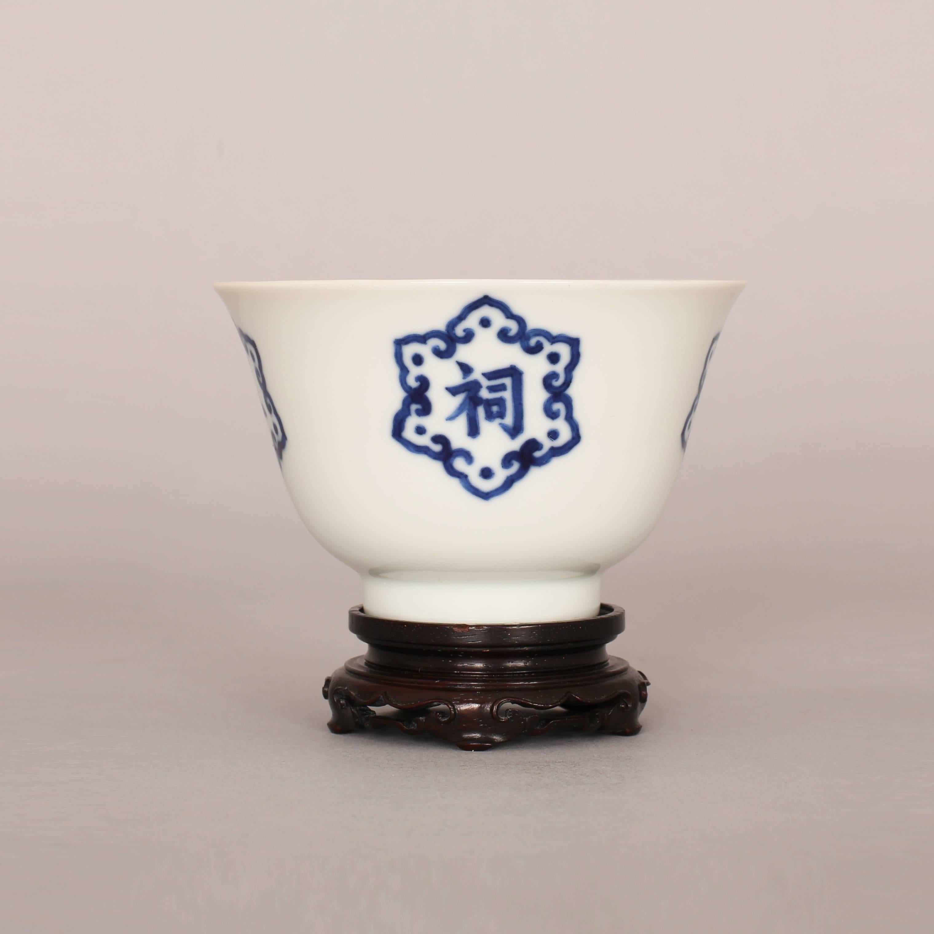 A Chinese porcelain blue and white wine cup with gently flared lip, painted with four six sided ruyi-head emblems containing ‘Wu Shi Zong Ci’ characters, the interior with a stylized decorative shou character, the underside with a six character mark