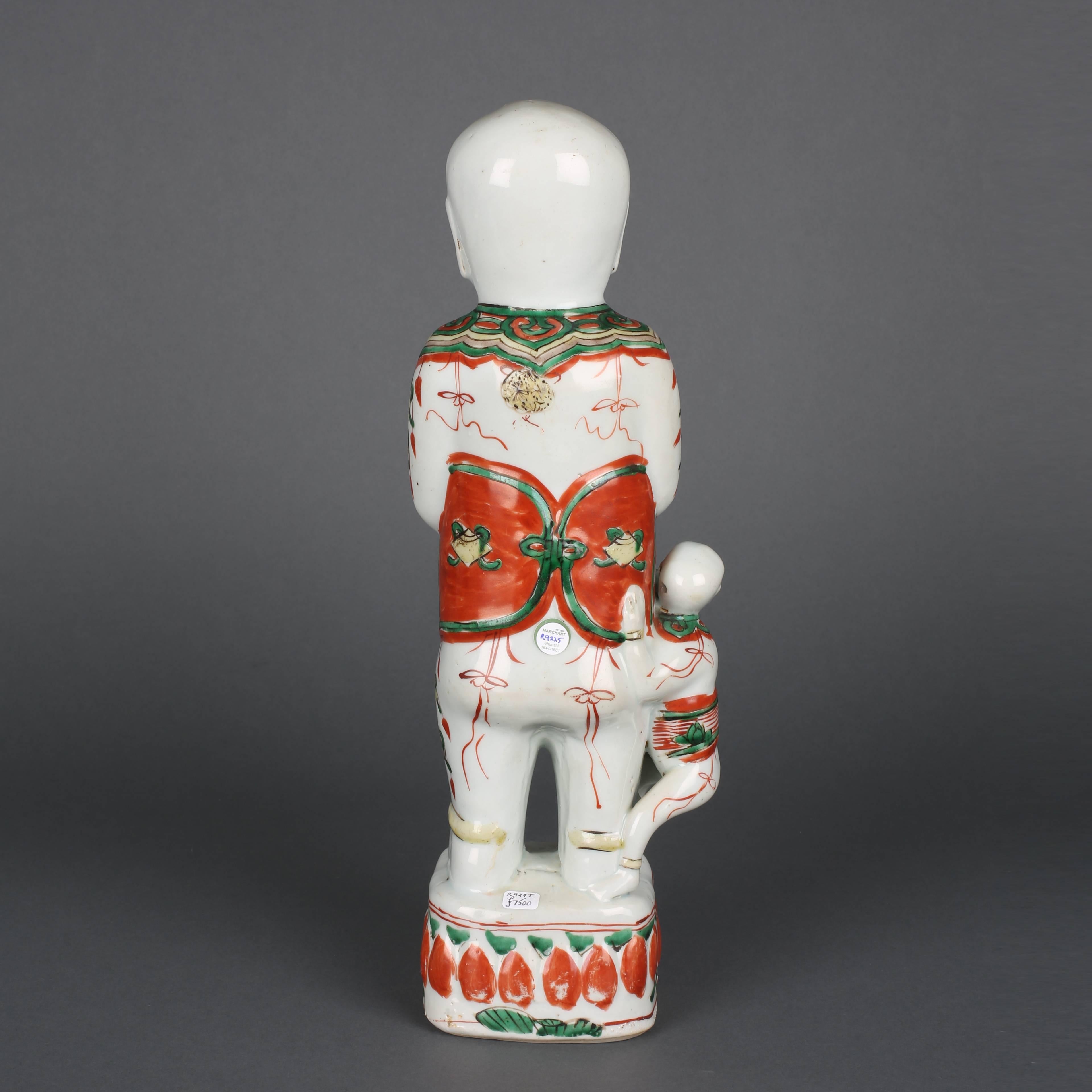 A Chinese porcelain famille verte large standing boy holding a vase while a smaller boy climbs his leg, all on a raised square base.

Measures: 34cm high, 8.5cm wide.

Shunzhi, 1644-1661.