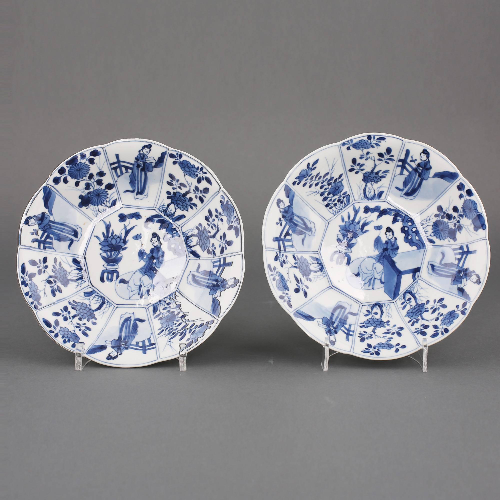 Pair of Chinese porcelain blue and white dishes with lobbed rims, the centres painted with a lady holding a lotus bloom while seated at a table beside a potted flowering lotus plant and rock work within a border of ten panels, four with ladies in a