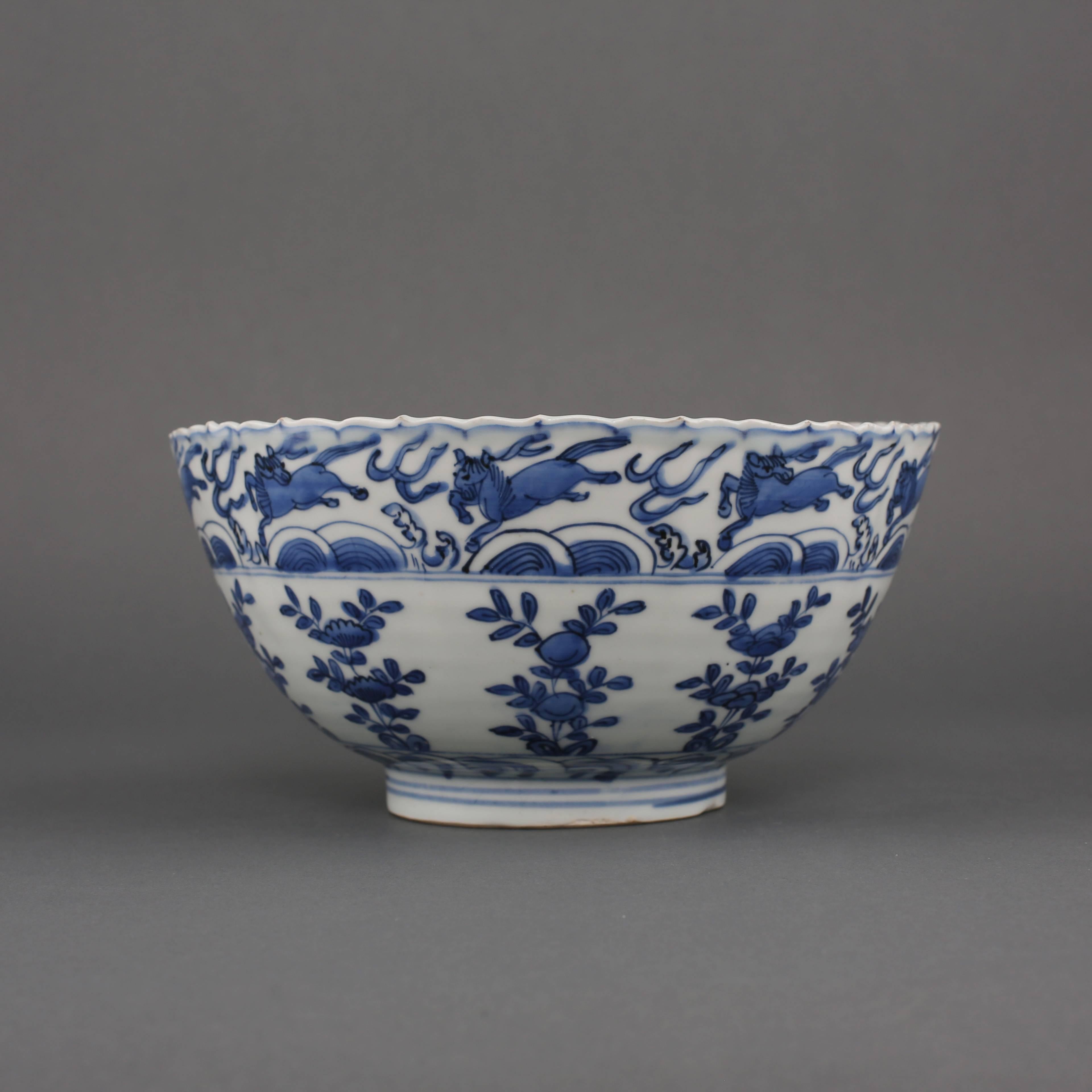 A Chinese Ming porcelain blue and white bowl with foliate rim painted with a wide band of horses jumping over waves, above ten upright alternating flowering and fruiting branches, between a continuous wave border at the base, the interior with a