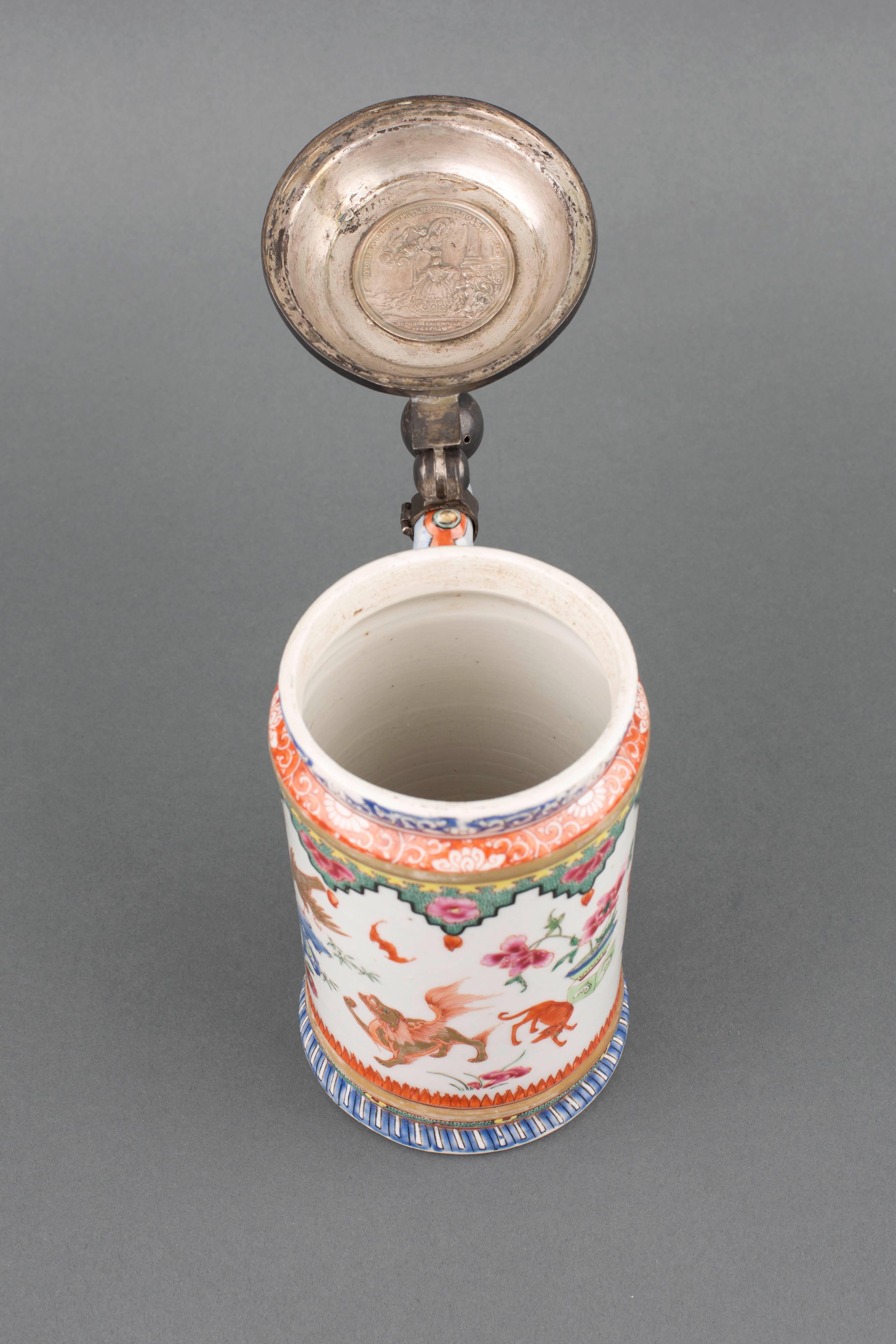 A Chinese export porcelain famille rose tankard with cylindrical body and splayed foot, the handle in the form of a dragon’s body with spine nodules protruding, painted in colored enamels with iron red and gilt with a n open-mouthed cockerel