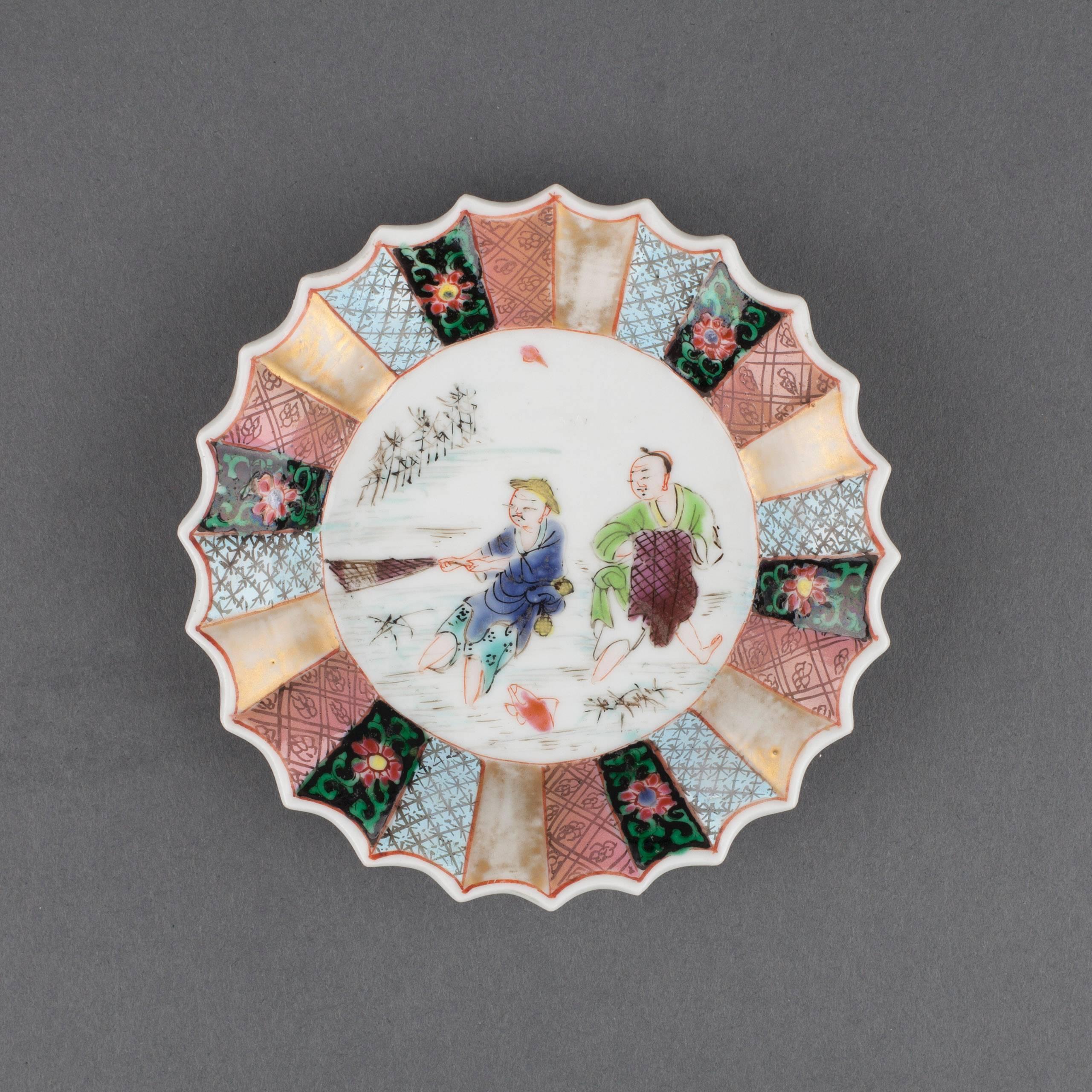 Chinese porcelain famille rose tea bowl and saucer of fluted petal form, painted in the centre with two fishermen standing in water, amongst reeds and a fish, one hauling a net, the other holding a net, all within an alternating panelled border of