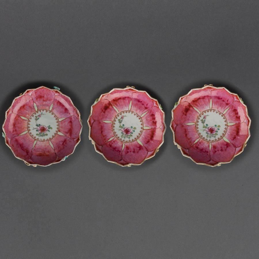 A set of three Chinese porcelain famille rose tea bowls and saucers in the form of lotus leaves, the exterior of the cups and underside of the saucers in relief with flowering lotus branches and foliage on a ground of graduating red lotus petals,