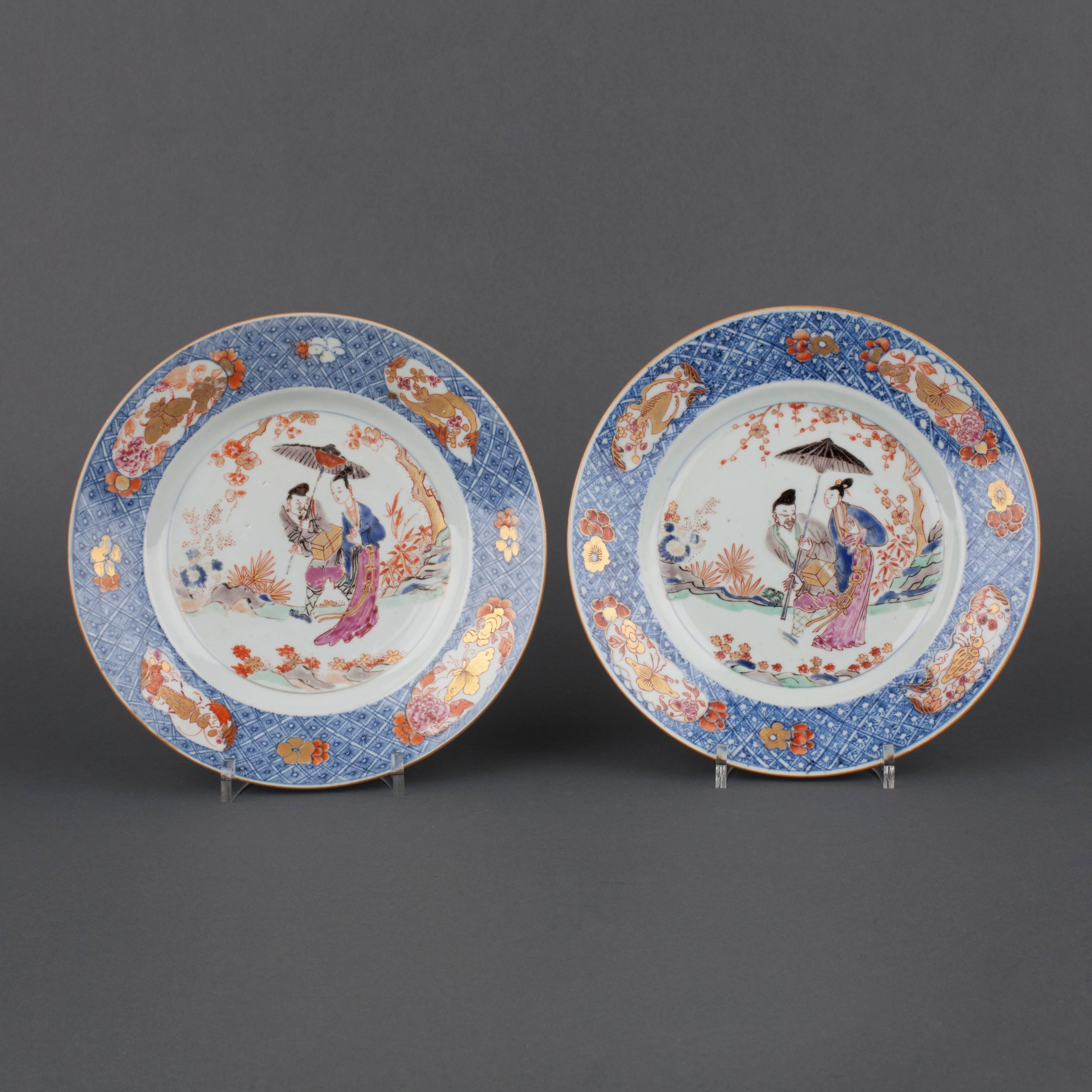 A pair of Chinese porcelain Madame au Parasol circular plates painted in famille rose enamels, iron red, gilt and underglaze blue, with a standing lady wearing long flowing robes, beside a male attendant holding a parasol and a box and cover, in a