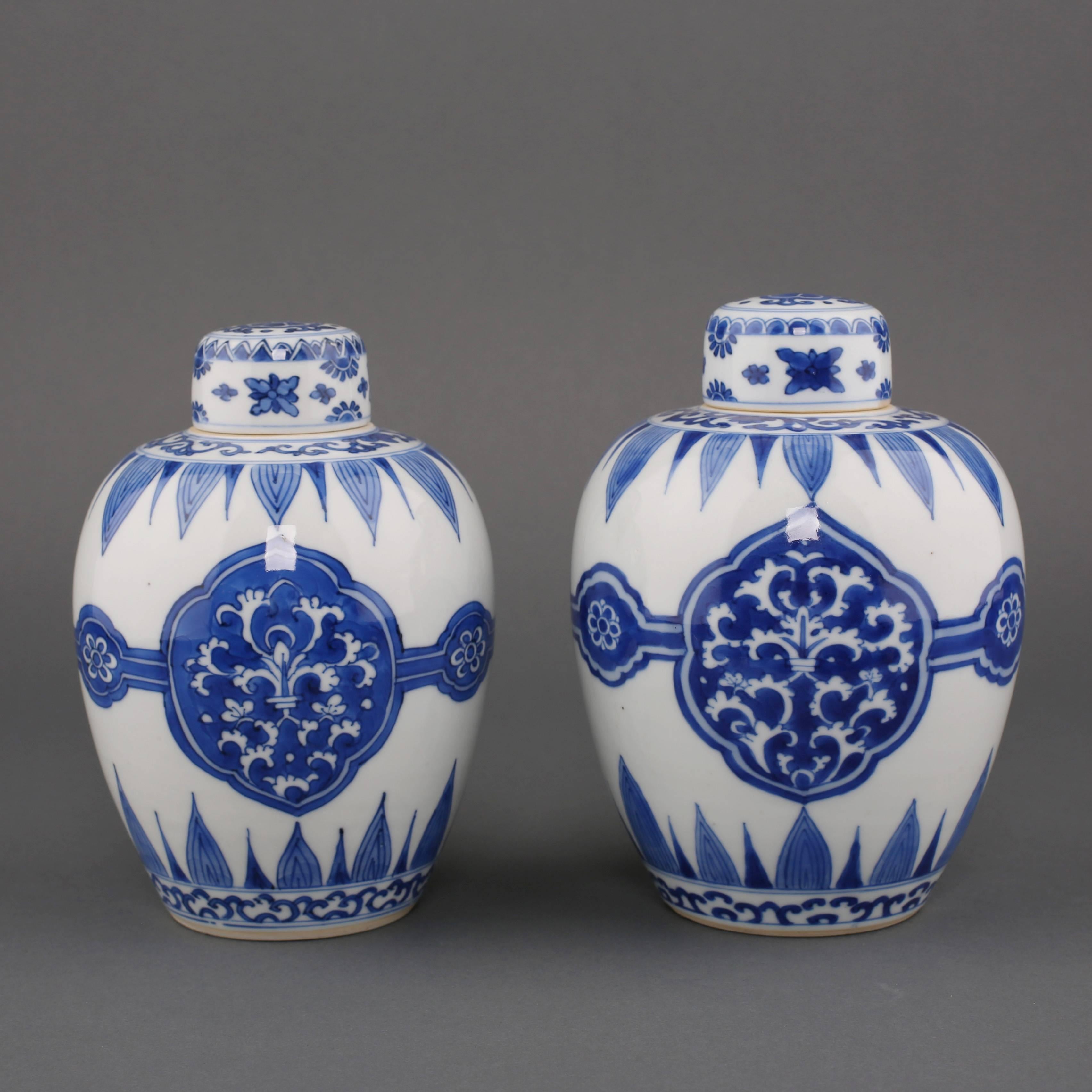 A pair of Chinese porcelain blue and white ovoid jars and covers, painted on either side with a stylized leaf motif enclosed in a panel, connected on either side by a small stylized flower head, all between alternating petal patterns and a further