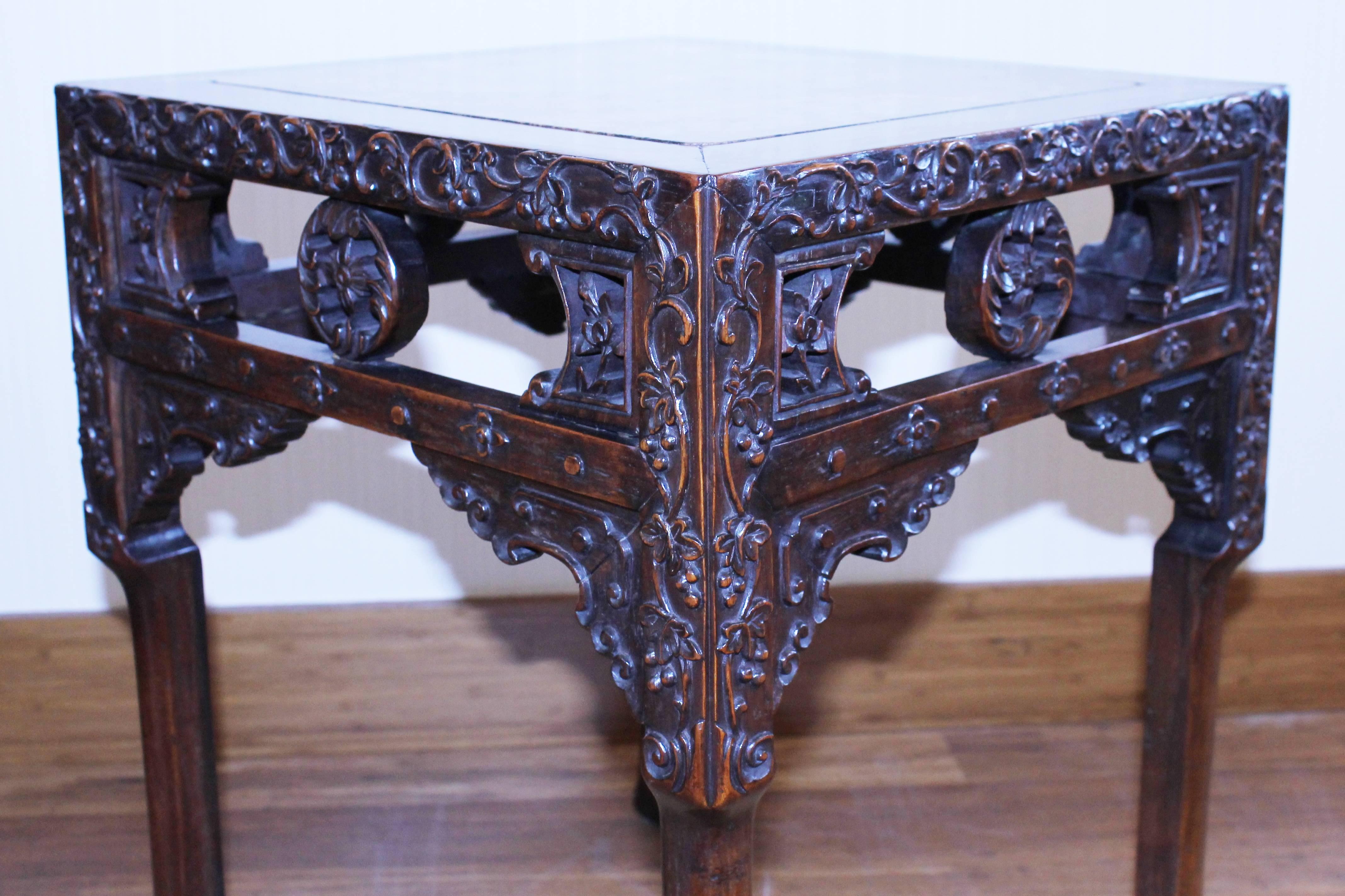 A Chinese hong-mu 'blackwood' square pedestal table, the top inset with a mottled pink marble, carved on the frieze in relief extending halfway down the leg with scrolling grapes and vine, with cross-stretcher carved with flower heads and dots, and