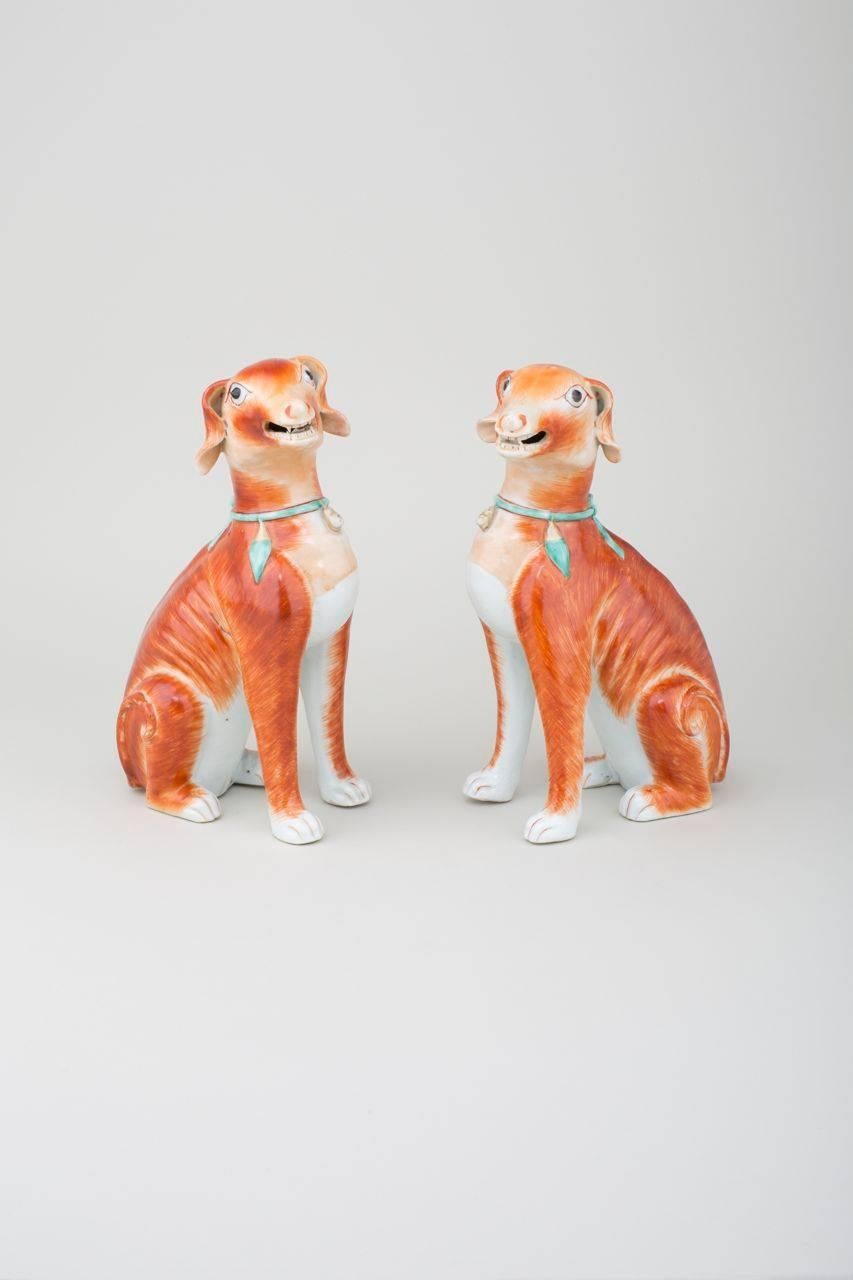 A pair of Chinese export porcelain iron-red seated open-mouthed hounds with pronounced spines, ribs and upright curled tails, with white glaze on the inside of the legs, paws and chests, turquoise-enamelled tied collars, tassels and bells heightened