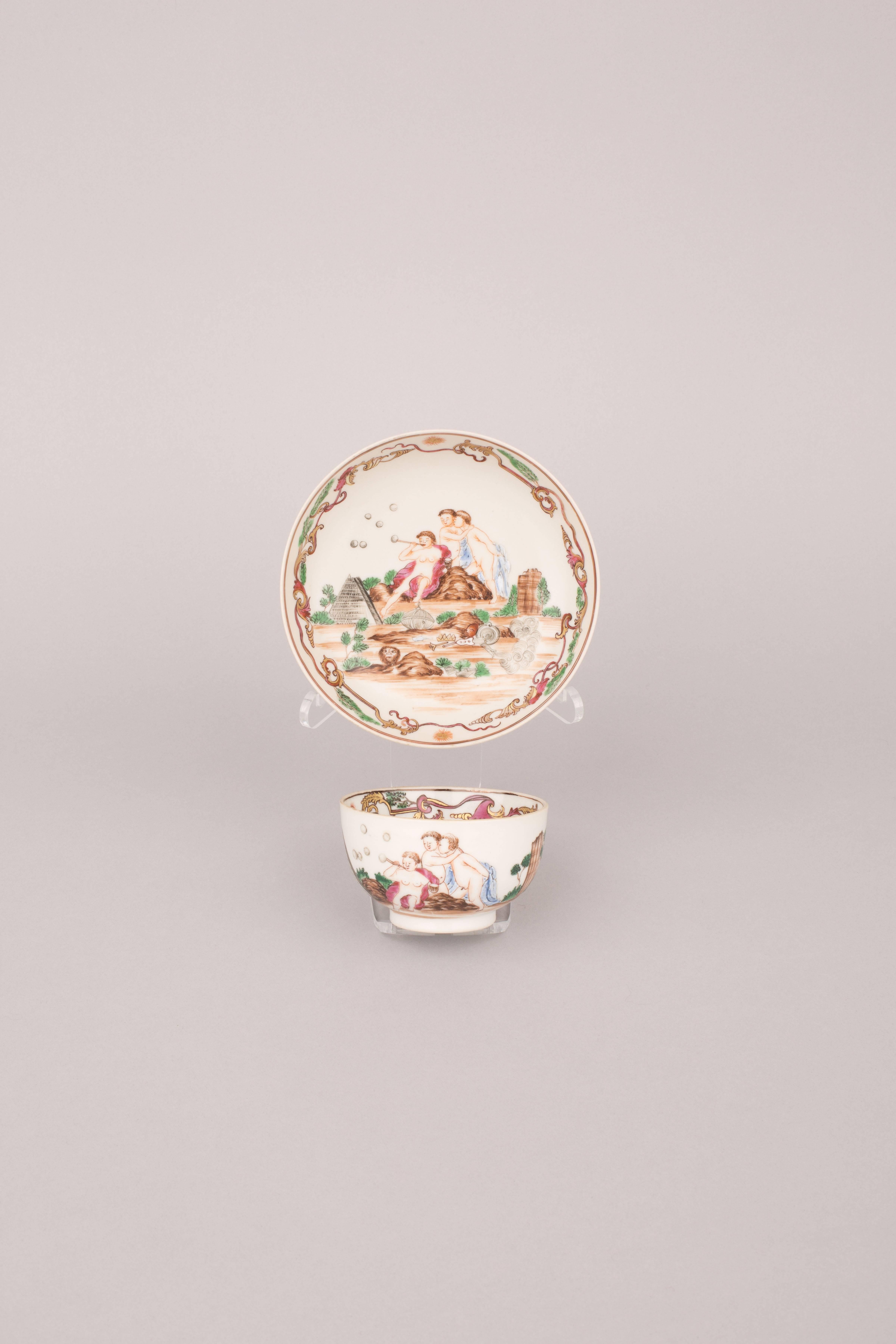 Famille rose tea bowl and saucer, painted after an unknown European engraving with three cherubs amongst rockwork, one blowing bubbles, the others embracing, beside a stone pyramid and discarded objects including a coronet, basket, palette, brush