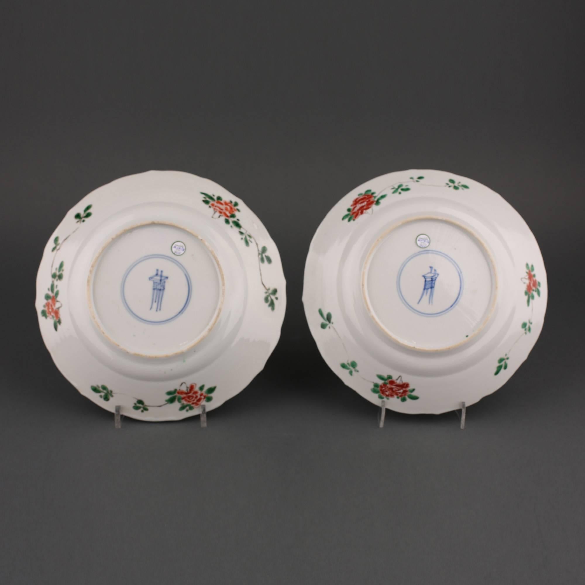A pair of Chinese porcelain famille verte circular lobed rim plates, the centre painted with peonies and pomegranate plants emerging from rockwork, butterfly and insects above, all within a six-panelled border of flowering plants on various diaper