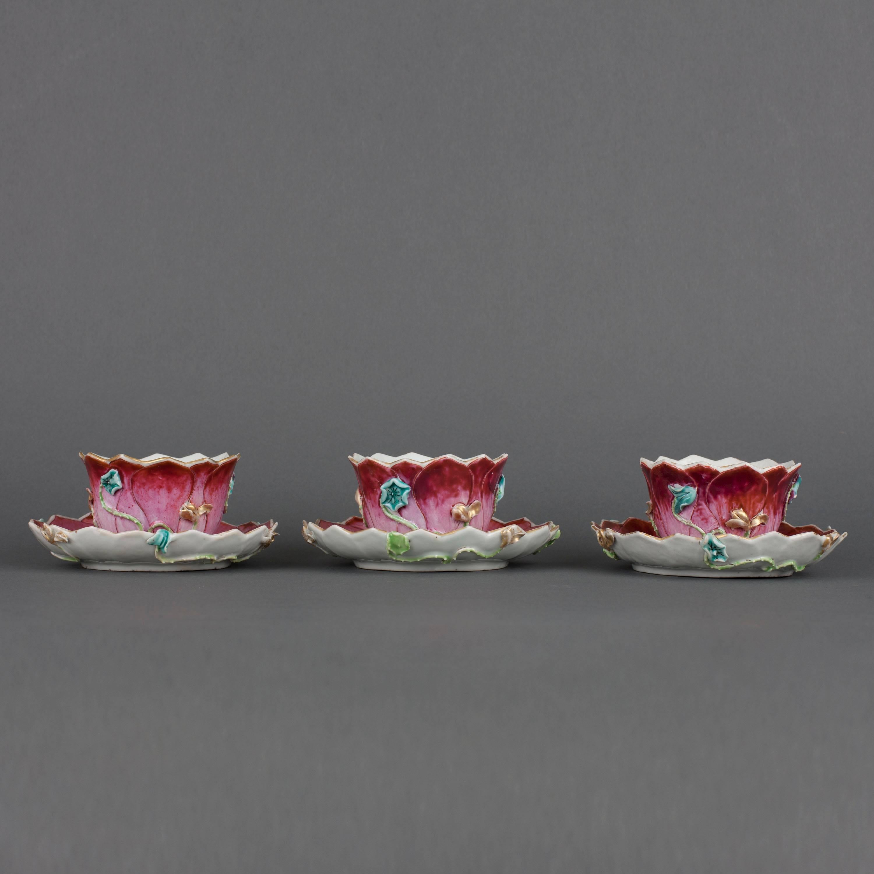 A set of three Chinese porcelain famille rose tea bowls and saucers in the form of lotus leaves, the exterior of the cups and underside of the saucers in relief with flowering lotus branches and foliage on a ground of graduating red lotus petals,
