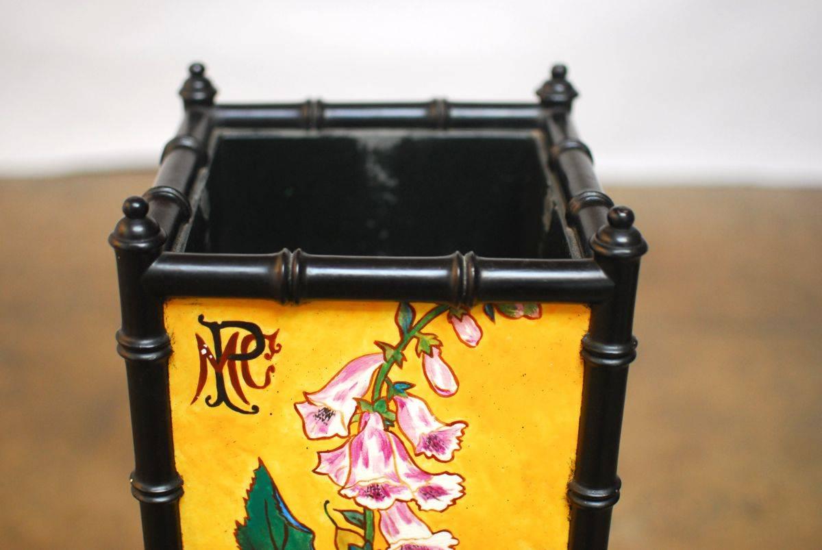 Elegant faux bamboo chinoiserie jardiniere constructed of wood with an ebonized lacquer finish. Features hand-painted porcelain tiles on each side depicting colorful spring flowers on a bright yellow background, signed by the artist. The long