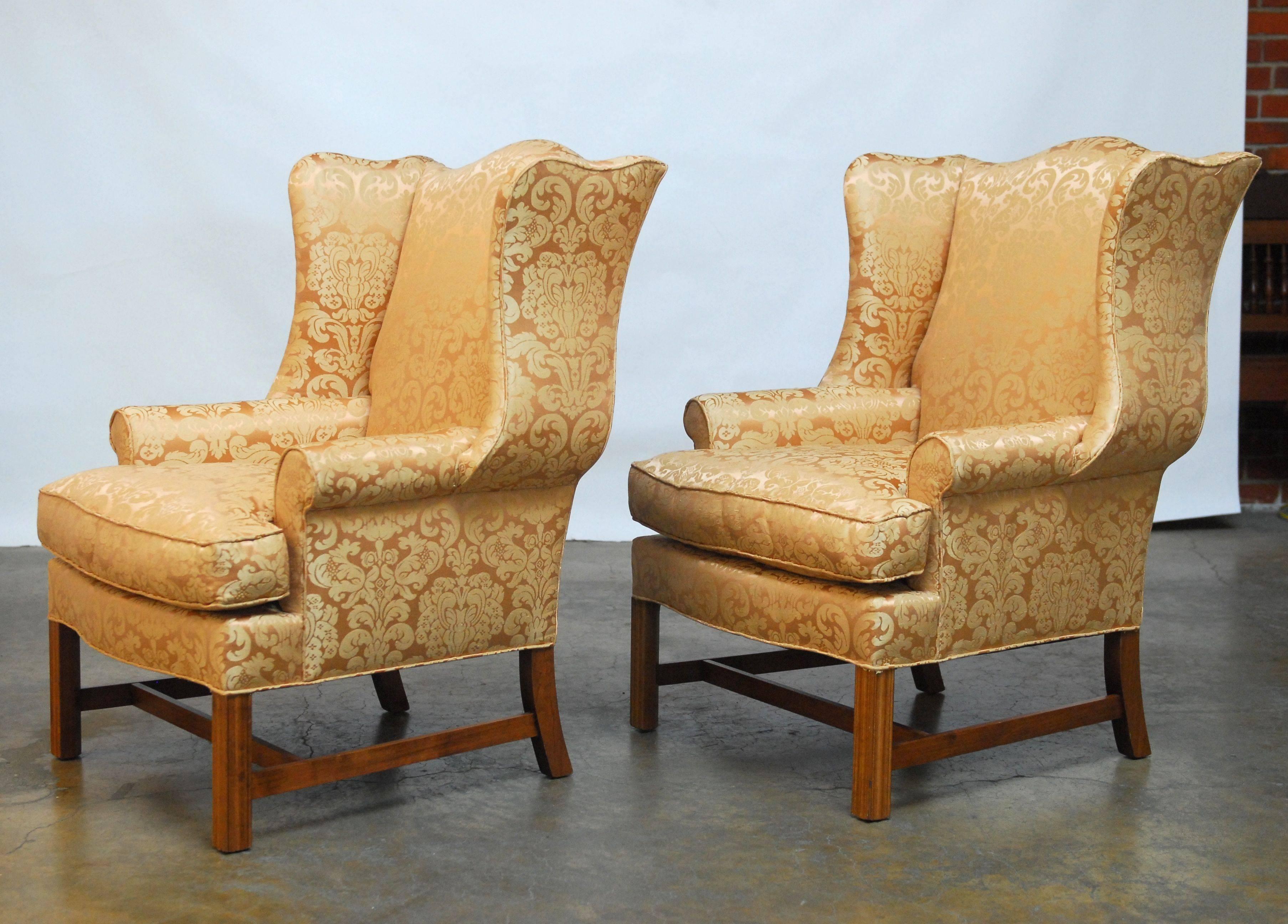 Pair of gorgeous wingback chairs with fully developed serpentine wings and generous proportions. Featuring a rose quartz color damascus silk upholstery. Supported by square chamfered molded legs with a cross stretcher. These chairs were recently