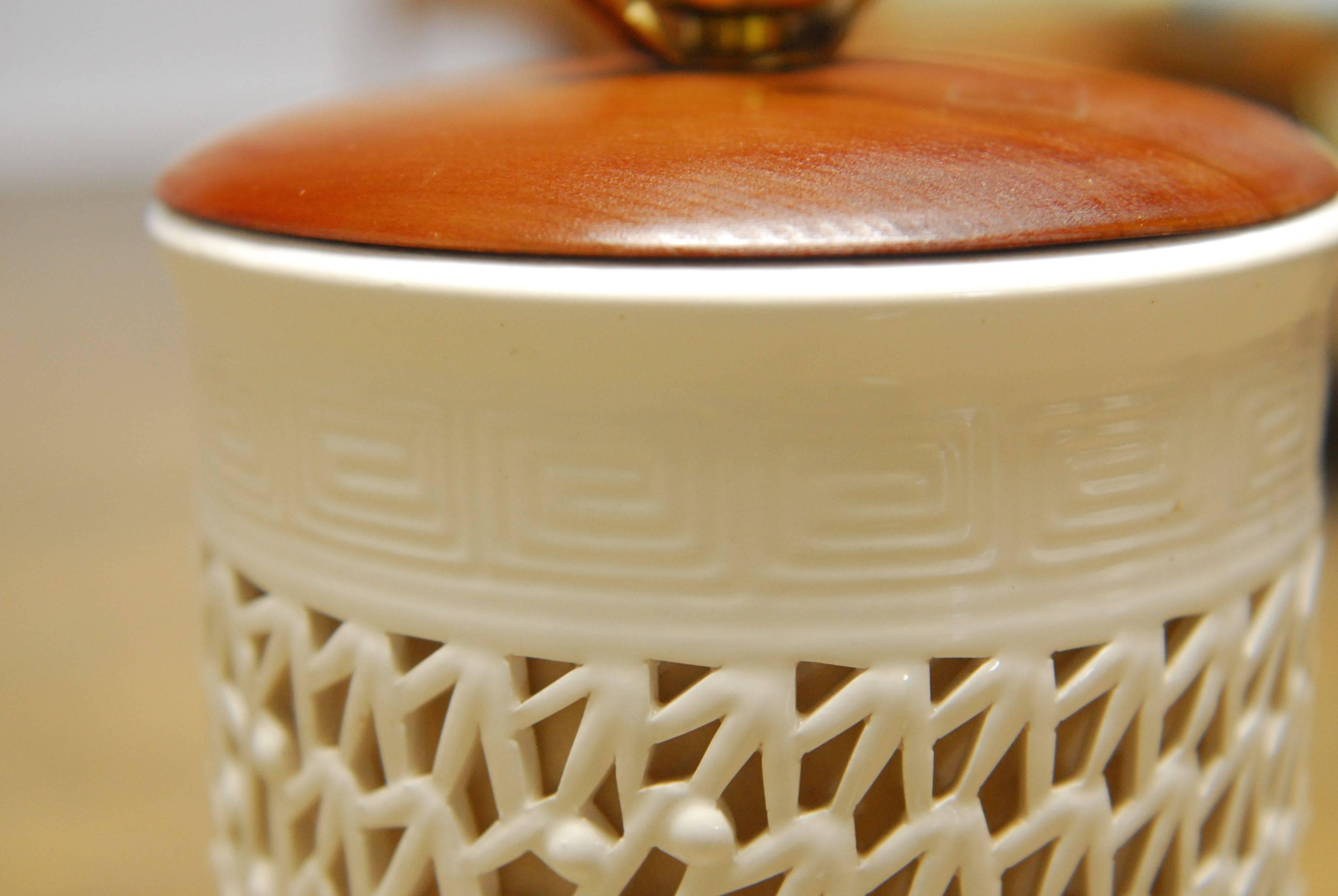Blanc de Chine table lamp with a delicate pierced work porcelain in a cylinder form. The top and bottom of the porcelain are decorated with a subtle Greek key band and sits on a carved wood base. The body is lined with rice paper that allows light