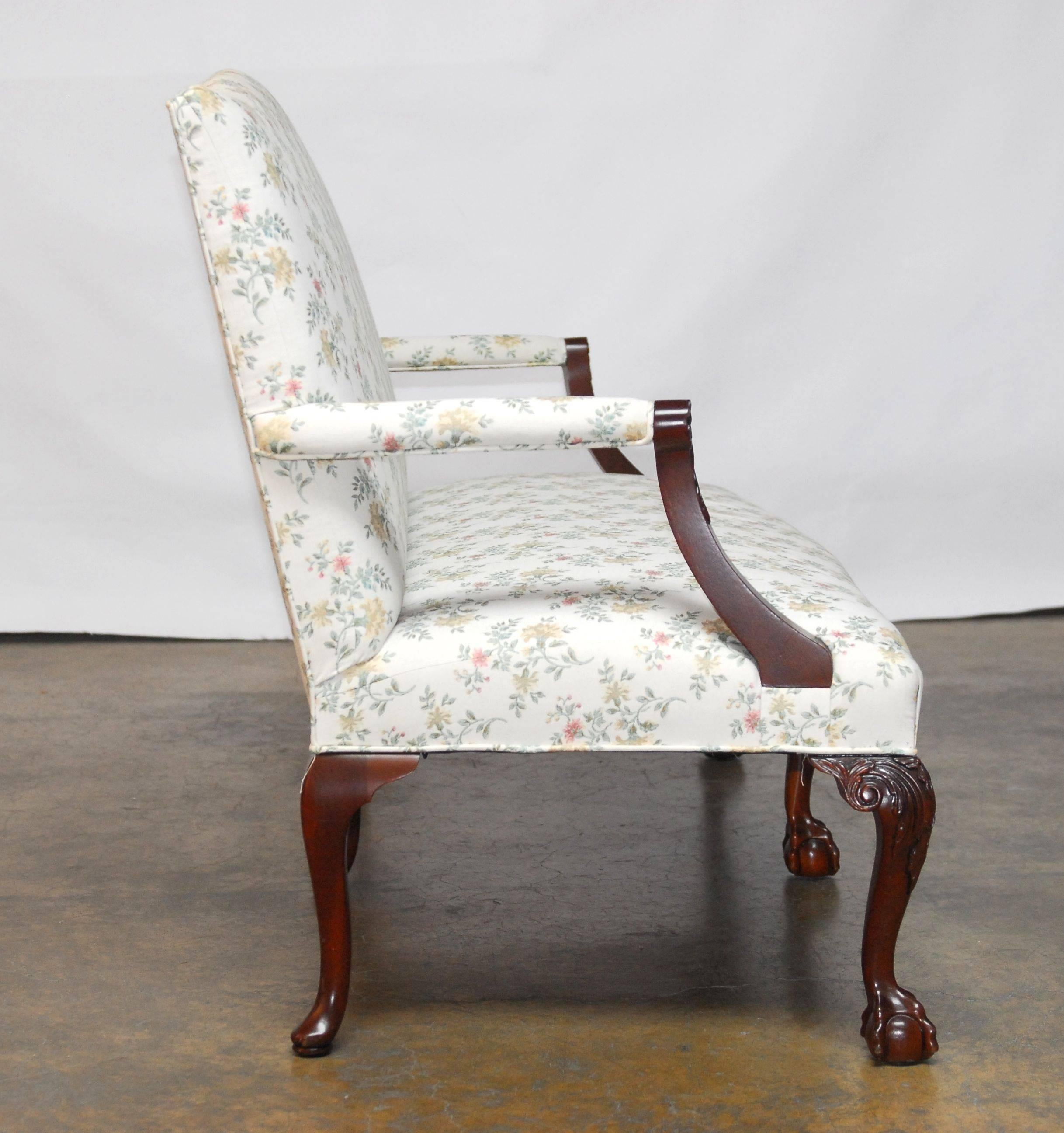 Distinctive mahogany settee made in the George II taste featuring six cabriole legs with the front carved in the Thomas Chippendale Ball and Claw style. The settee has a serpentine crest and bow front and is upholstered in a floral print over a