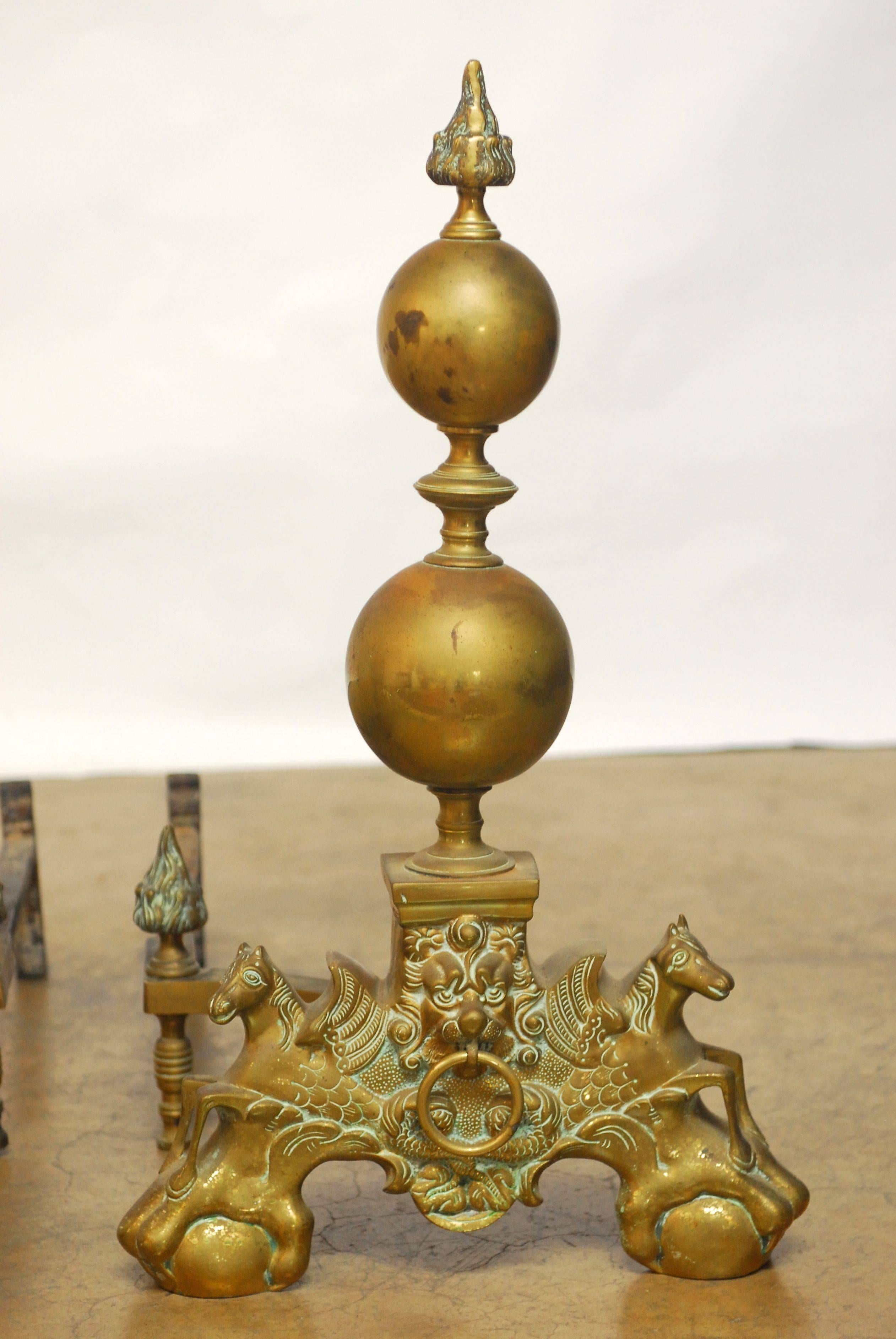 Exceptional pair of English andirons constructed of brass featuring large double cannonballs with flame finials. Each andiron flanked by winged seahorses and centered by a lion's head with a ring motif. Supported by stylized ball and claw feat and